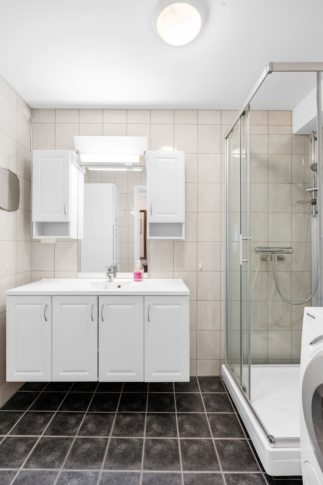 Badet er utstyrt med flislagte overflater, dusjkabinett og innredning med nedfelt servant. Galleribilde