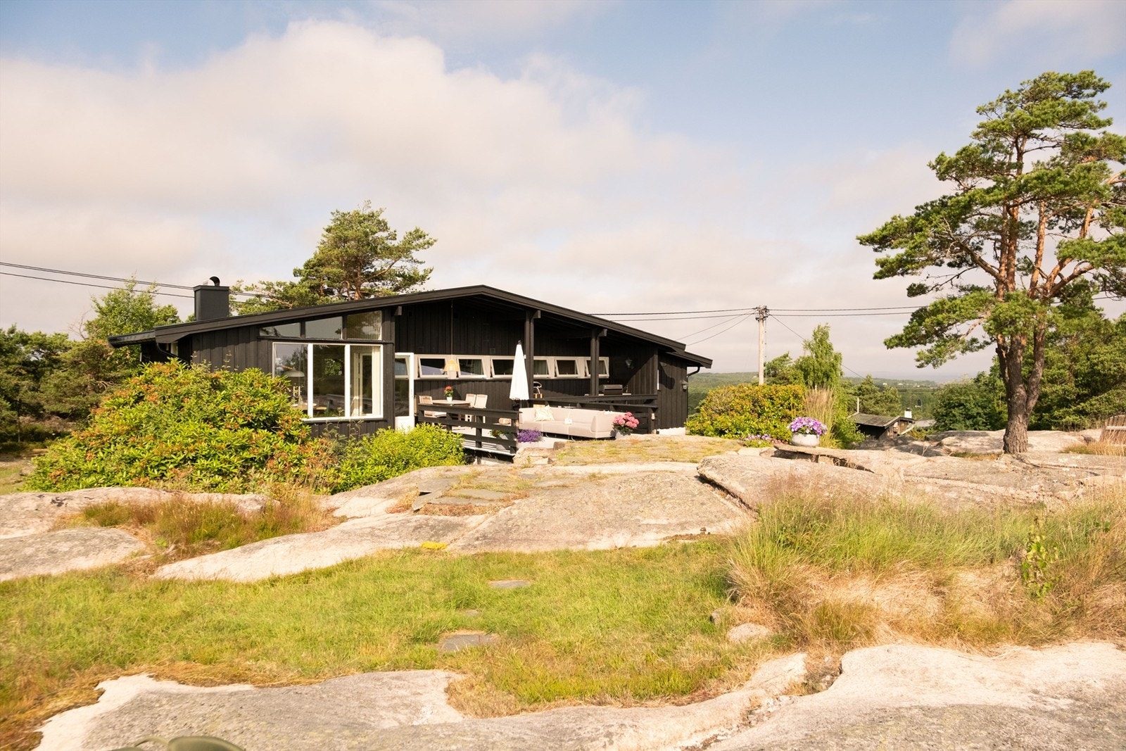 Den karakteristiske hytta smelter harmonisk inn i de naturlige omgivelsene, med svaberg, furutrær og en usjenert terrasse som inviterer til lange sommerdager i solen. Galleribilde