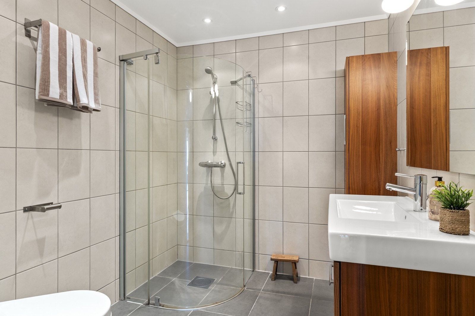 Badet i første etasje er helfliset og utstyrt med dusj med glassdører, vegghengt toalett og servantinnredning. Galleribilde