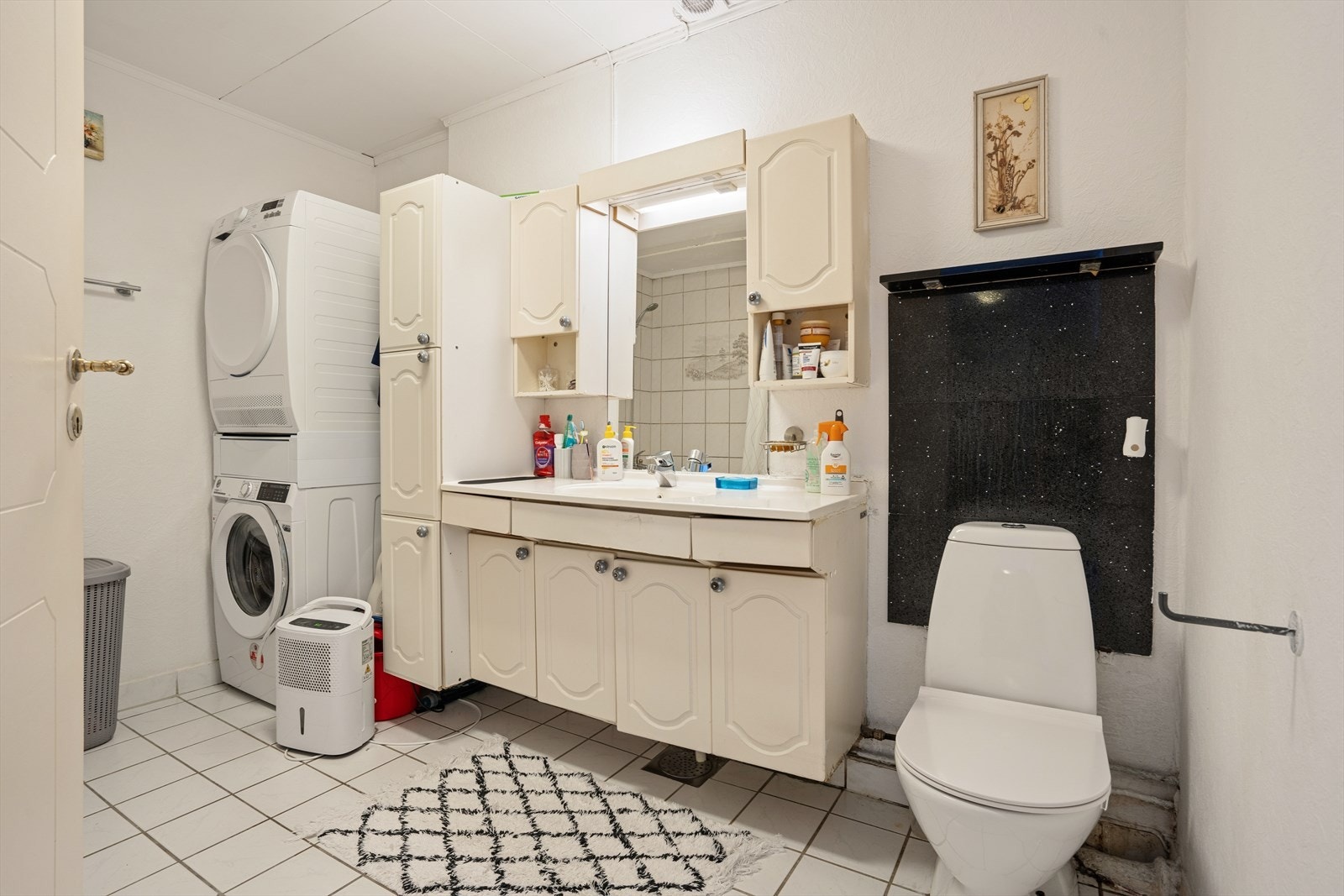 Eldre, flislagt bad med elektriske varmekabler i gulvet, badekar og praktisk opplegg for vaskemaskin. Galleribilde