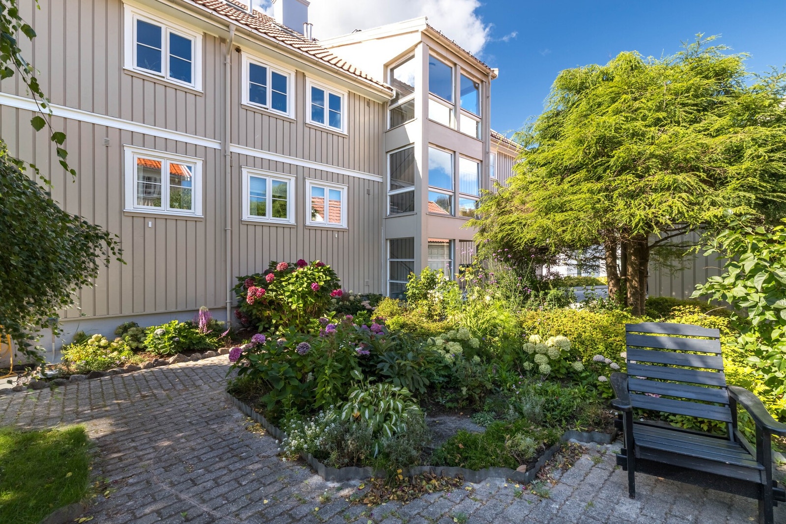 Bakgården mellom byggene i sameiet er pent opparbeidet med ulike planter, blomstre og trær Galleribilde