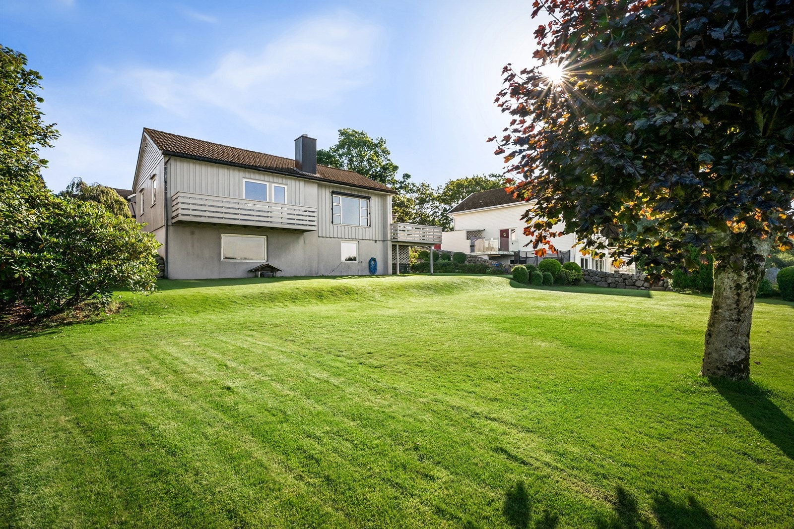 Eiendommen har en stor, grønn plen som strekker seg ned mot vannet. Galleribilde