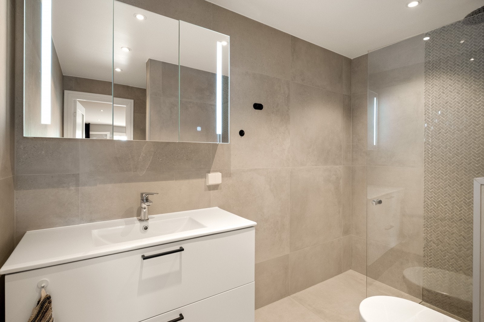Badet har flislagte vegger og gulv, malt tak og behagelige varmekabler. Innredningen består av benkeskap med slette fronter, laminatbenkeplate og veggskap med speil og belysning Galleribilde