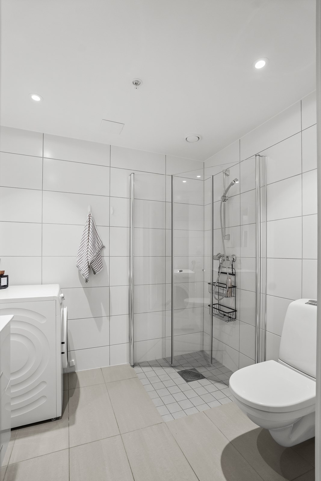 Videre er badet utstyrt med veggmontert toalett og et praktisk dusjhjørne med innfellbare glassvegger. Det er også opplegg for vaskemaskin, noe som gjør hverdagen enklere. Galleribilde