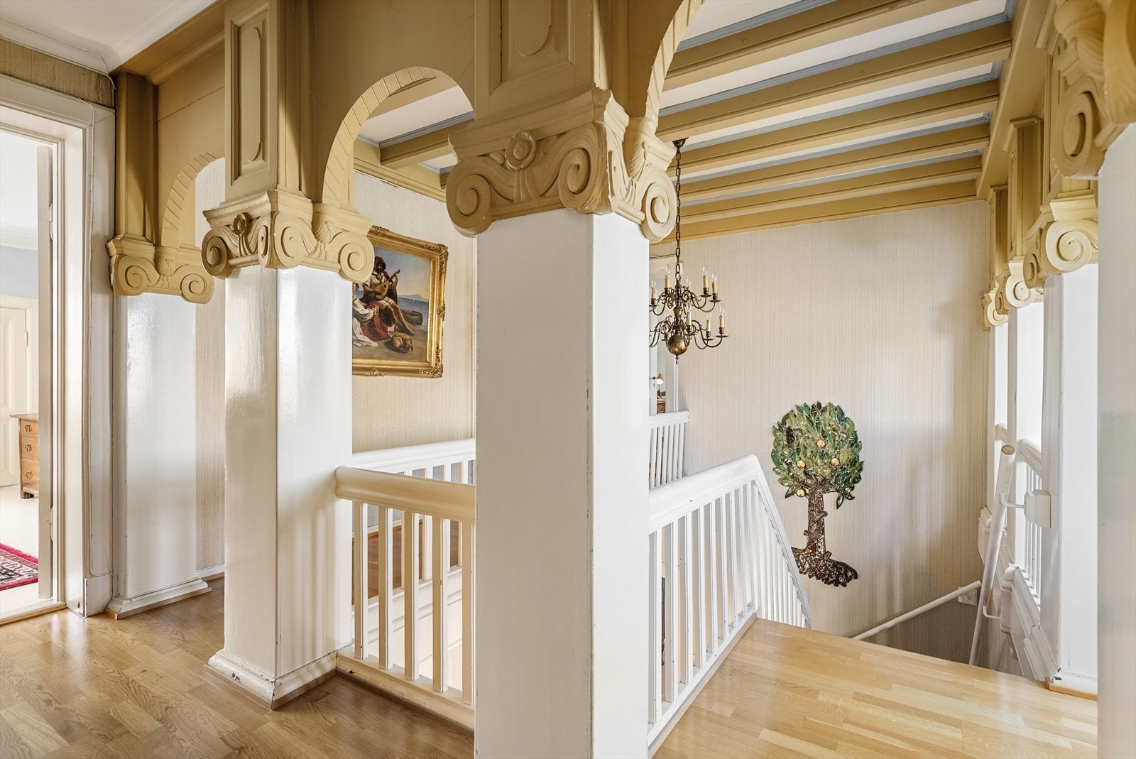 Trappehallen fremstår som et naturlig blikkfang i boligen, med dekorative søyler, elegante buer og flotte håndverksmessige detaljer som vitner om husets historie og sjel Galleribilde