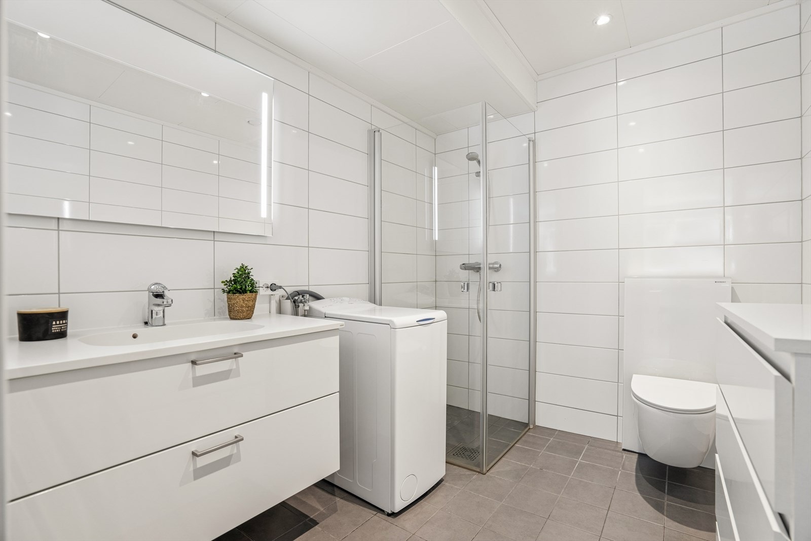 Badet i hybeldelen har flislagte overflater, varmekabler i gulvet og opplegg for vaskemaskin. Galleribilde