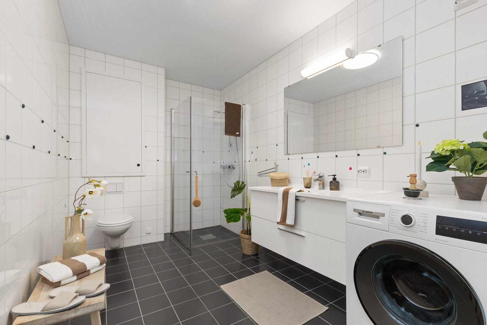 Flislagt bad med gulvvarme, vegghengt servantinnredning og opplegg for vaskemaskin. Galleribilde