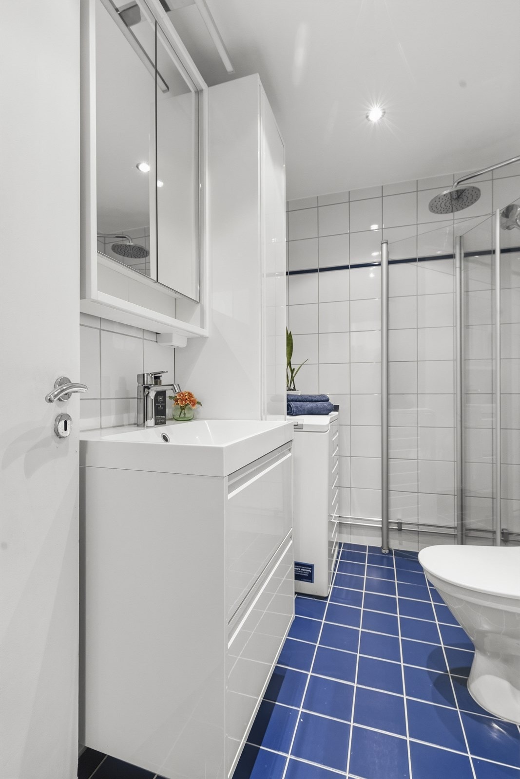 Badet er innredet med vegghengt servantinnredning og skap, speil med overlys, dusjhjørne med glassdører og gulvstående toalett Galleribilde