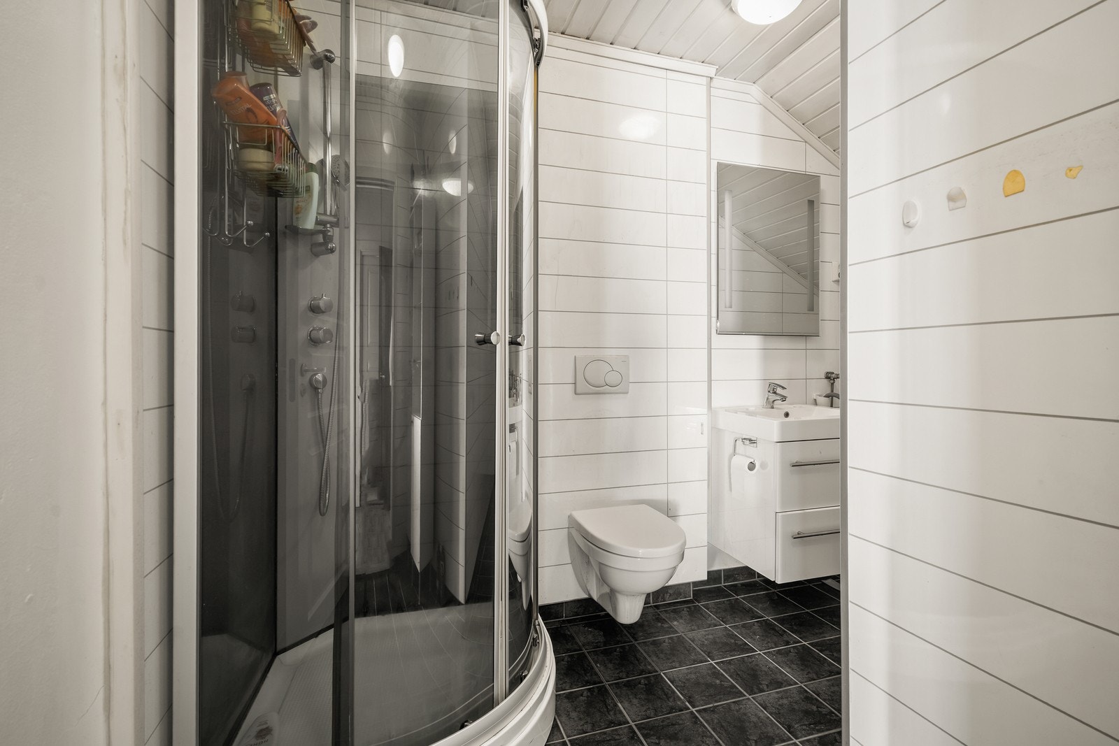 Badet i 2.etasjen er utstyrt med dusjkabinett og vegghengt toalett og har mørke gulvfliser samt lyse, horisontale veggfliser. Galleribilde