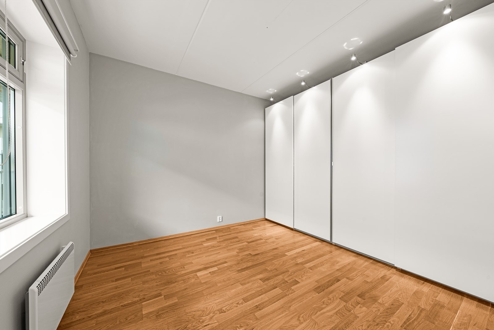 Langs den ene veggen er det en stor skyvedørsgarderobe med god oppbevaringsplass. Integrert belysning over garderoben bidrar til et stilrent uttrykk. Galleribilde