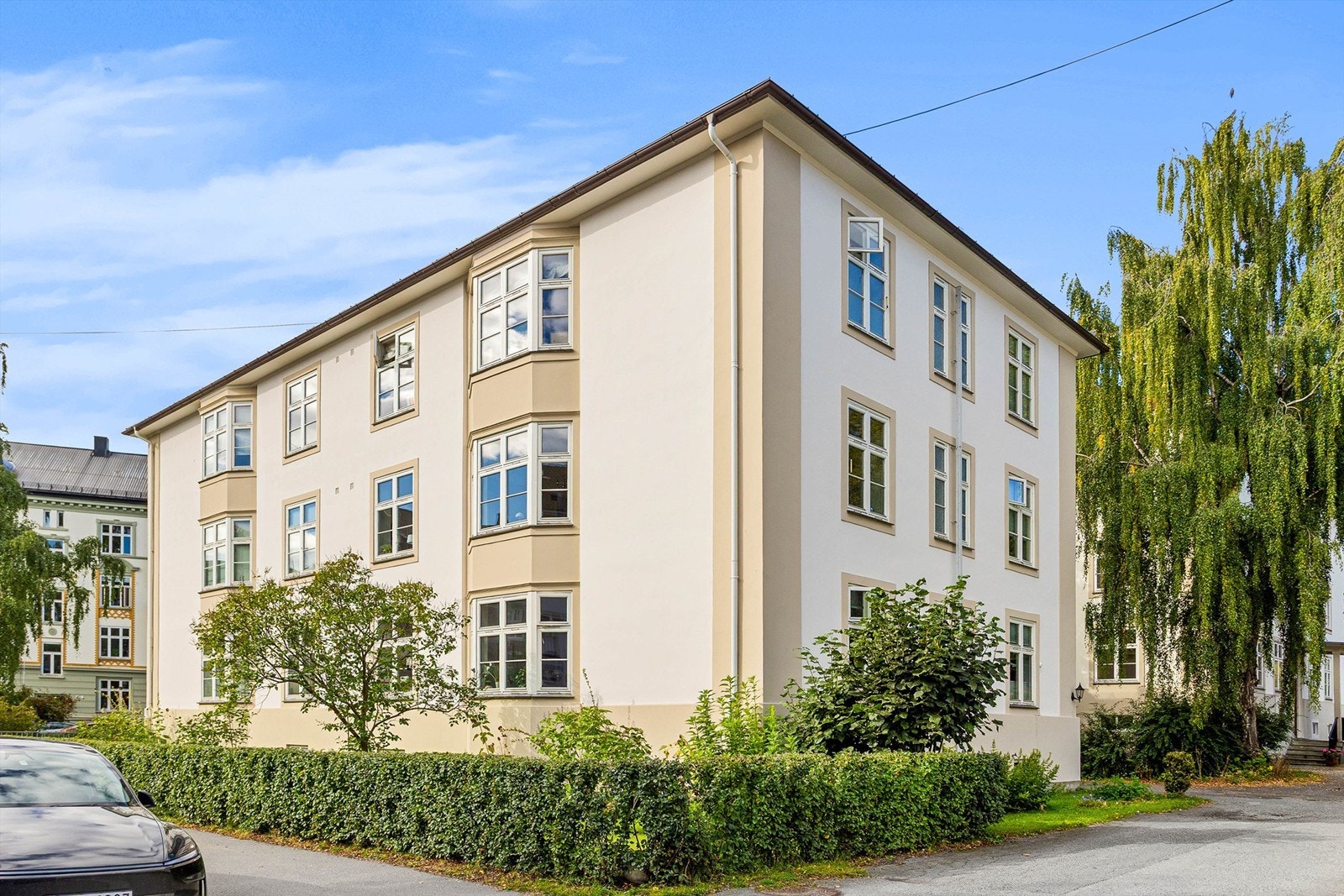 Staselig bygård fra 1933 med klassisk pusset fasade og en frodig, grønn hage. Galleribilde