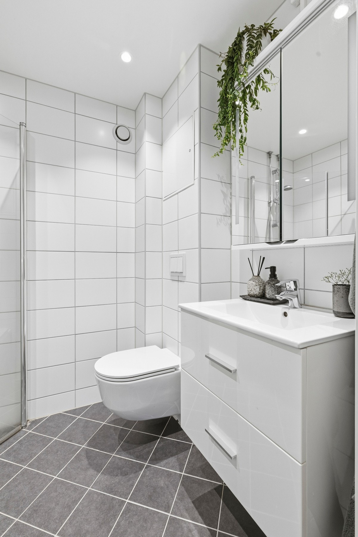 Badet er innredet med heldekkende servant, romslig underskap og speilskap med integrert belysning. I tillegg til veggmontert toalett, dusjhjørne med glassdører og praktisk opplegg for vaskemaskin. Galleribilde