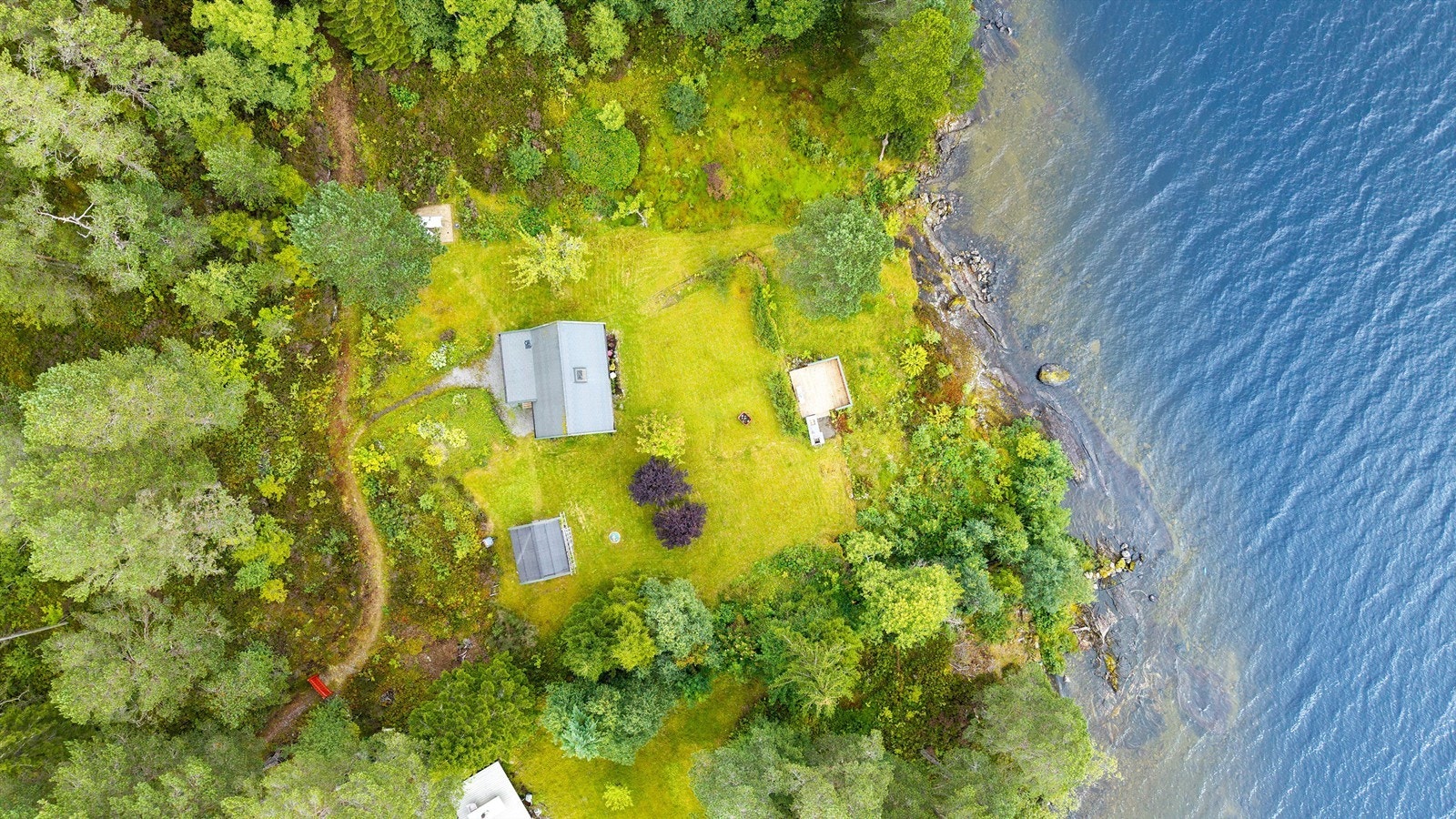 Eiendommen sett fra luften, med strandlinje og to terrasseplattinger. Galleribilde
