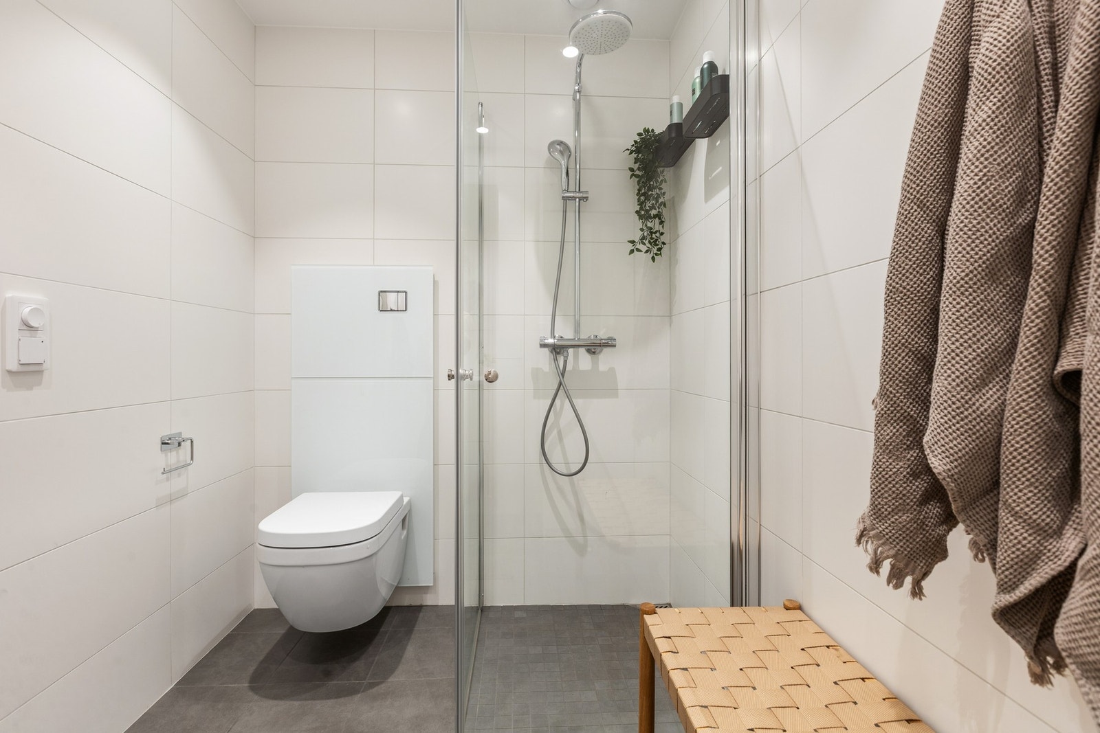 Rommet har et lyst og tidløst uttrykk, og er innredet med vegghengt servantinnredning med skuffer, speil, vegghengt toalett og dusjsone med glassdører. Galleribilde