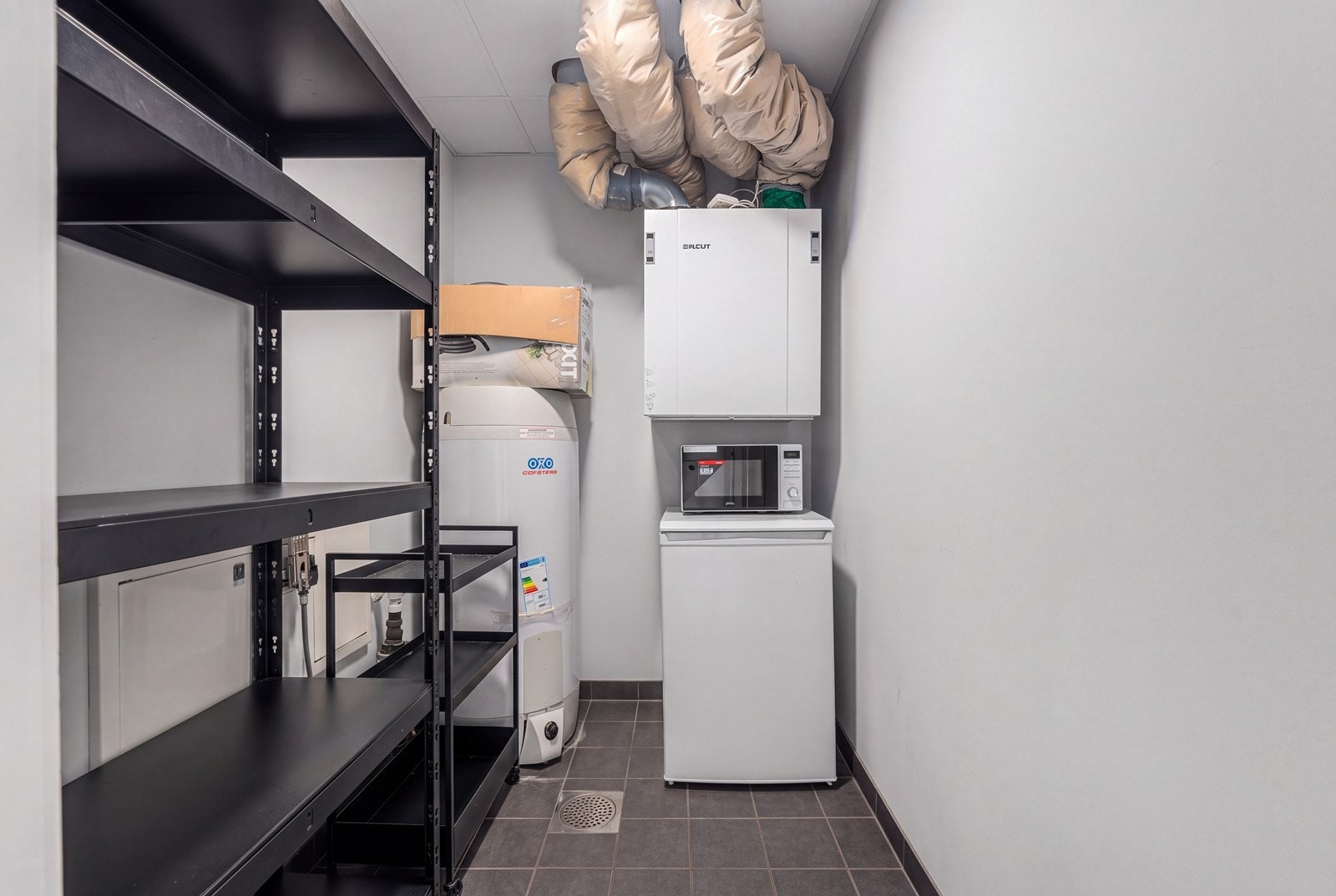 Innvendig bod med flislagt gulv, varmtvannsbereder og ventilasjonsaggregat. Galleribilde