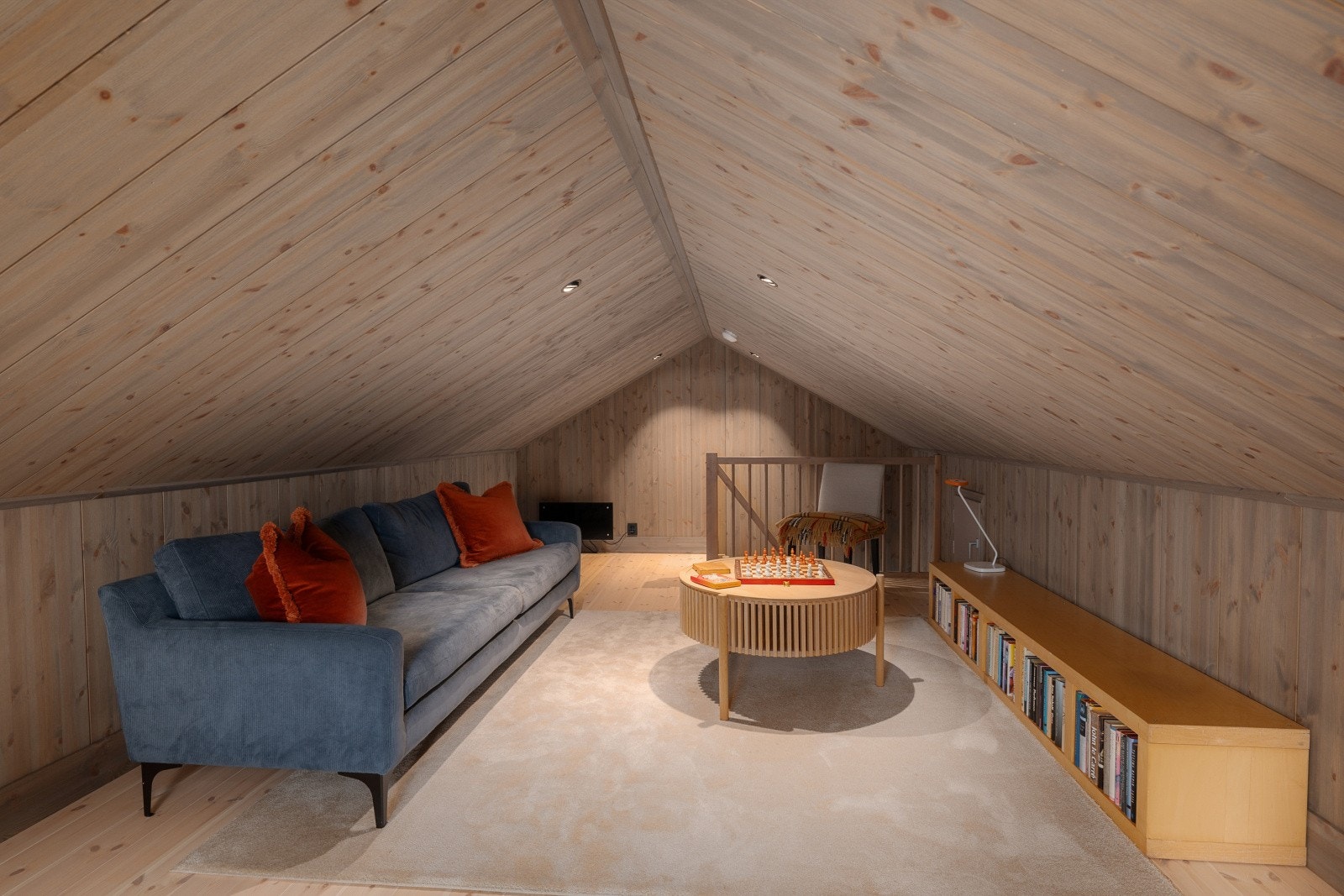 Trappen i treverk fører opp til hemsen, som er innredet med sofa og lave bokhyller. Galleribilde