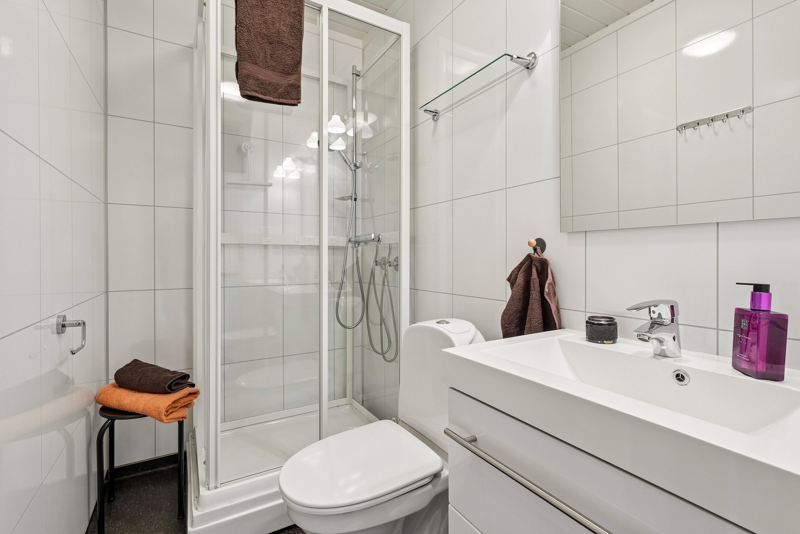 Badet har lyse baderomsplater på vegger og mørkt gulvbelegg med varmekabler Galleribilde