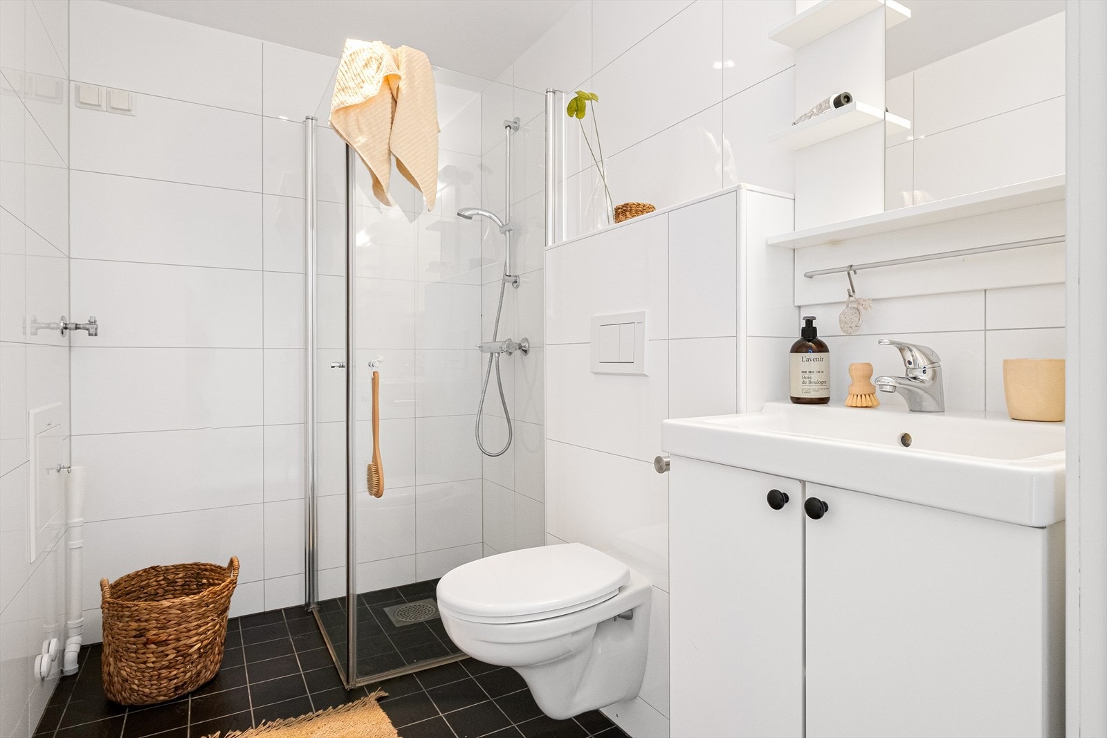 Flislagt bad/wc med varmekabler, avtrekk, speil, armatur, downlights, opplegg for vaskemaskin, servant med innredning, dusj hjørne med innfellbare glassdører, og vegghengt toalett. Galleribilde