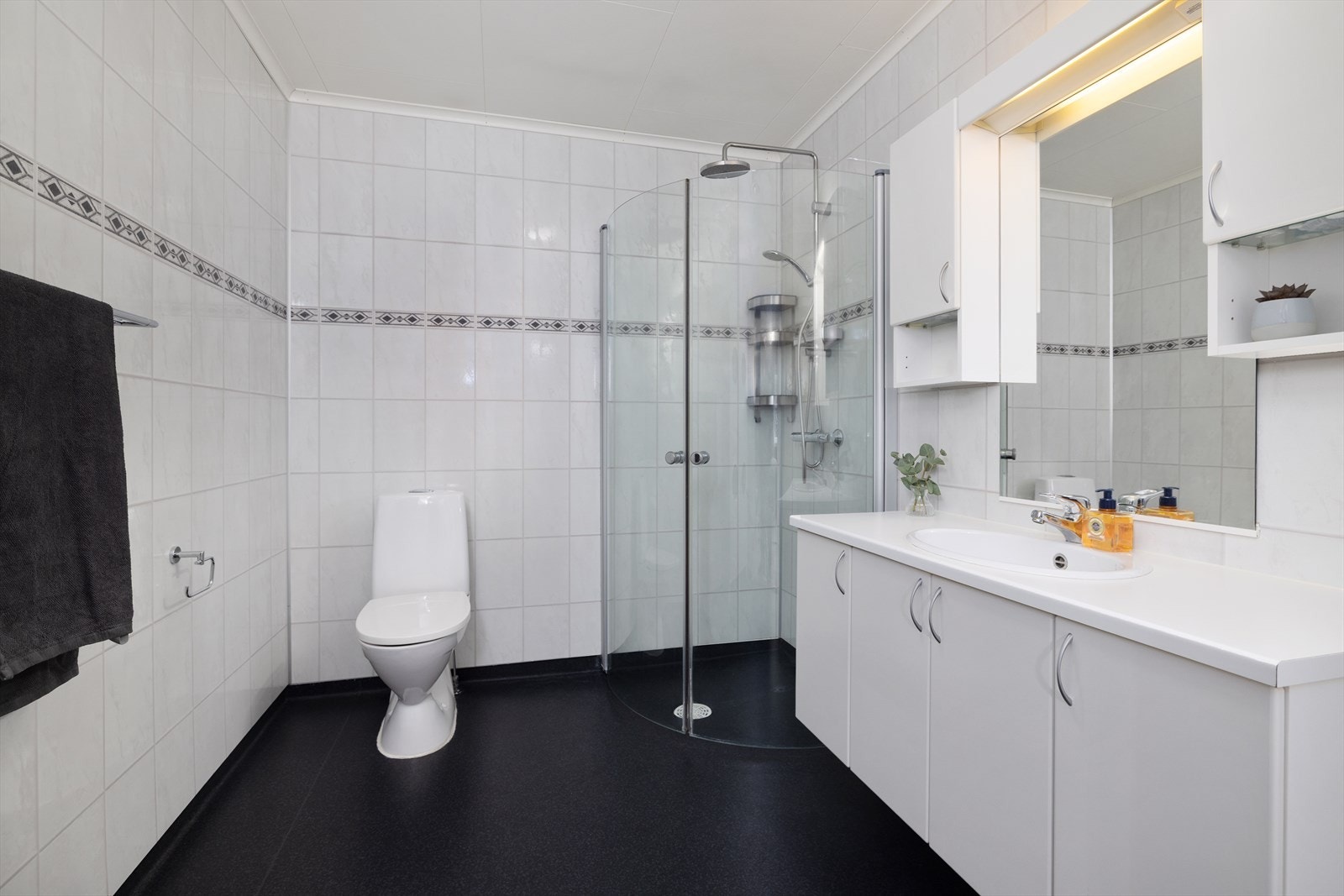 Dusjhjørne med glassdører. Badet har gulvbelegg og baderomsplater på vegg. Galleribilde
