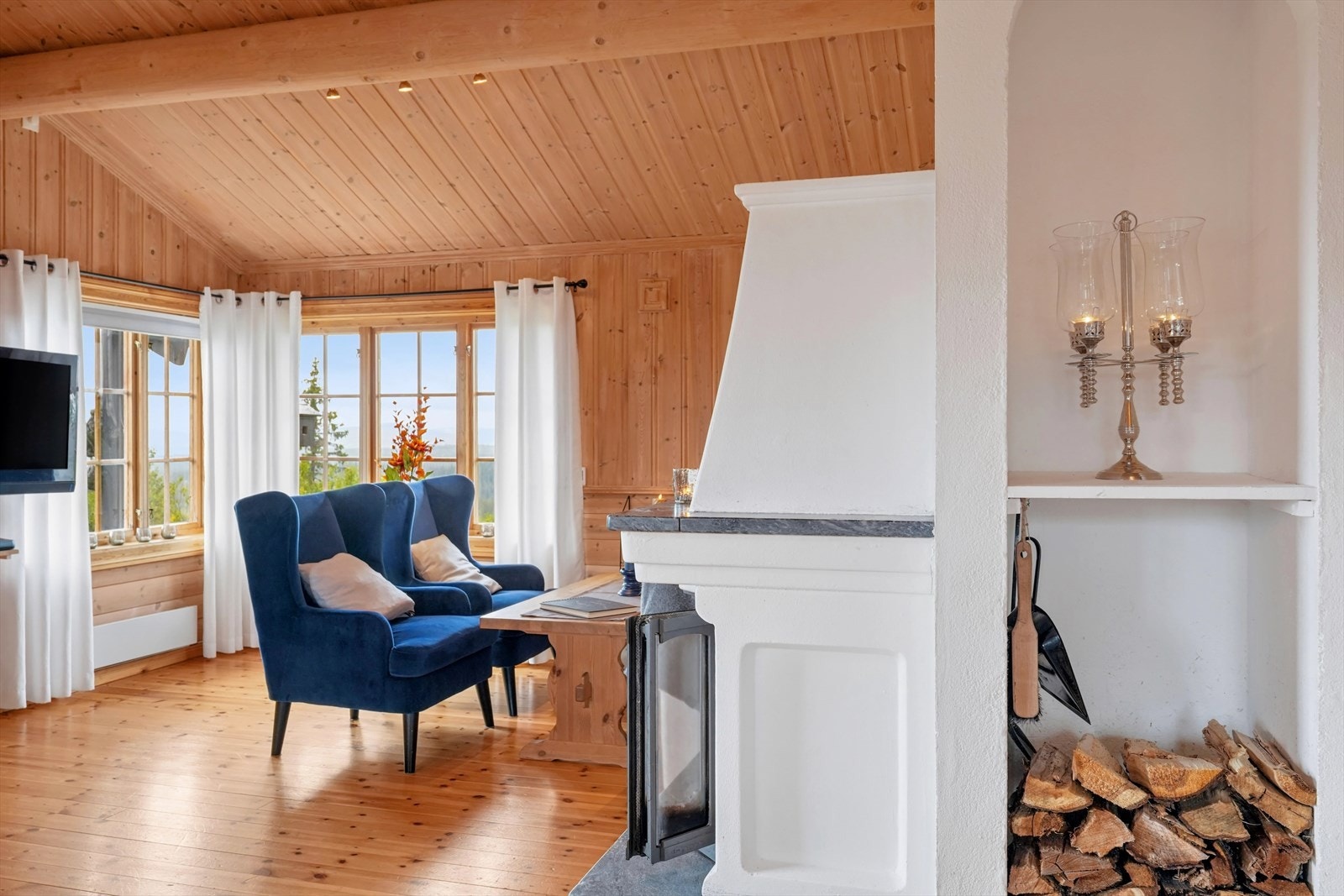 Koselig stue med synlige takåser i himlingen, murt peis med innsats og utsikt mot landskapet. Galleribilde