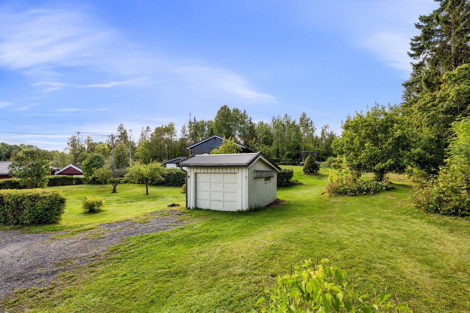 Stor og grønn tomt med plenarealer, frodig beplantning og frittstående garasje. Galleribilde
