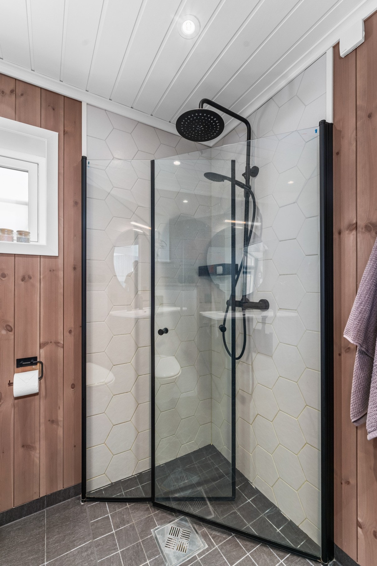Badet er utstyrt med veggmontert toalett og et romslig dusjhjørne med glassvegger og sorte armaturdetaljer. Galleribilde