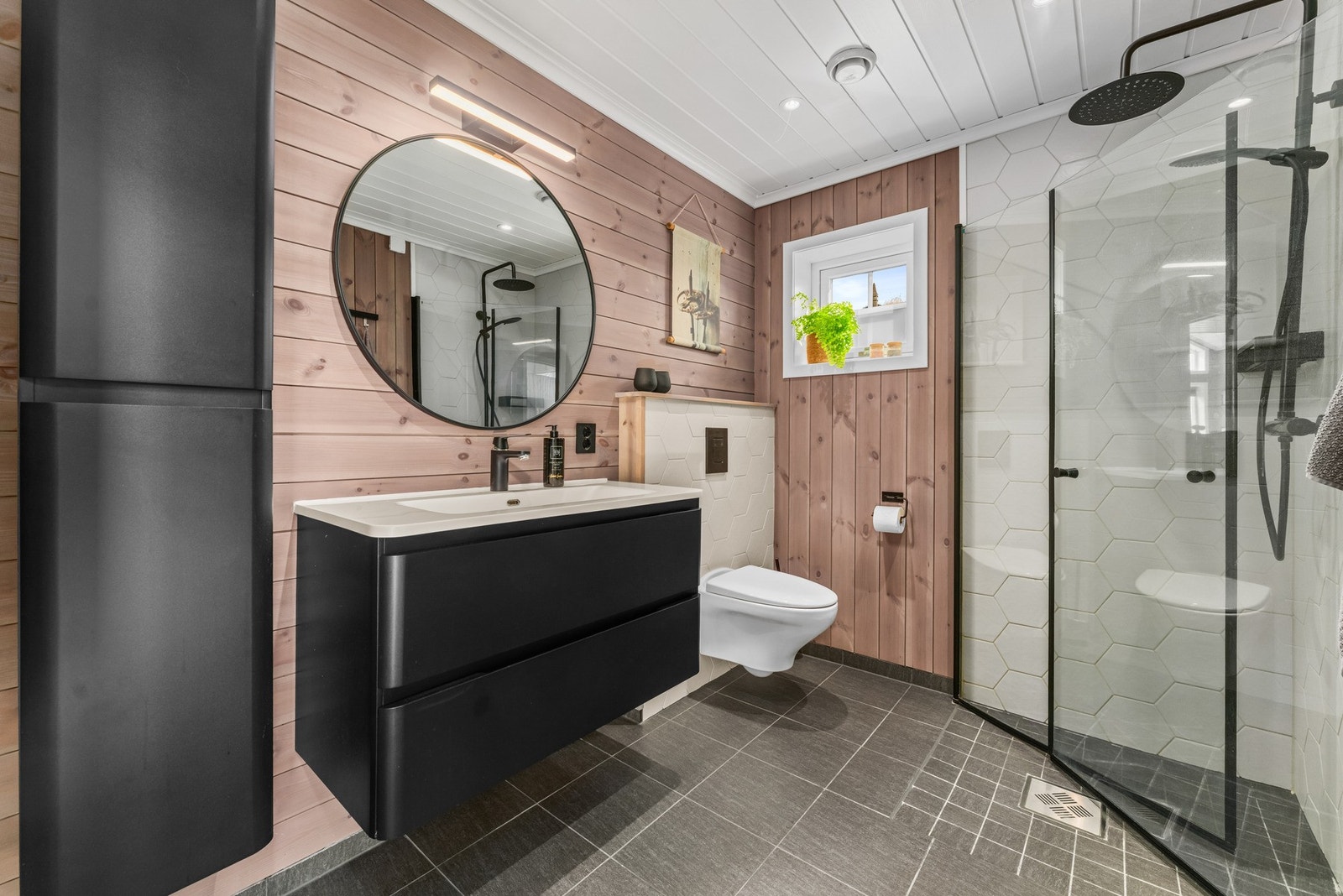 Badet har en moderne utførelse, hvor flislagte våtsoner kombineres med trepanel på øvrige veggflater og lysmalt panel i himlingen. Galleribilde