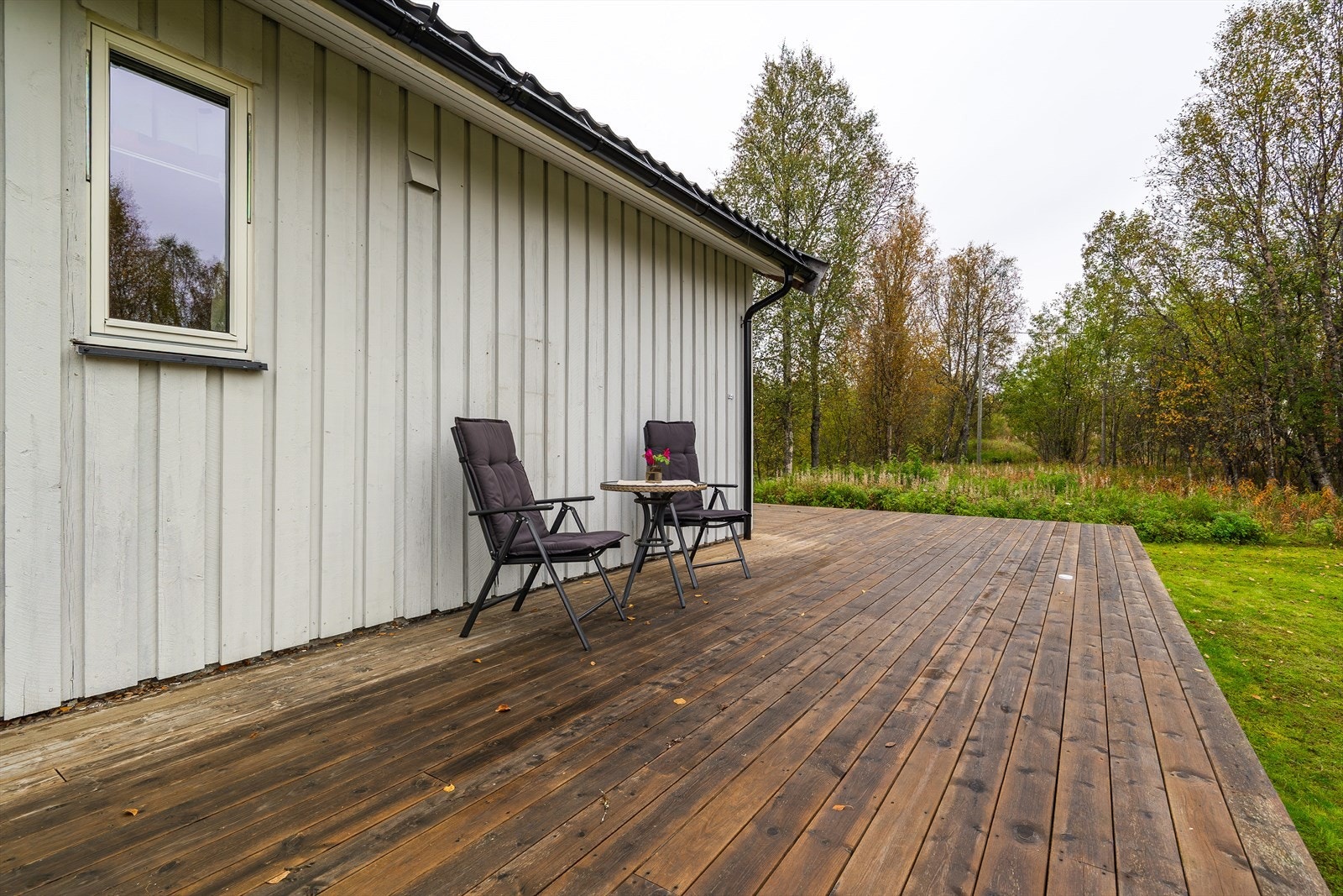Trebearbeidet platting på bakkenivå som grenser mot hage og plenareal. Galleribilde