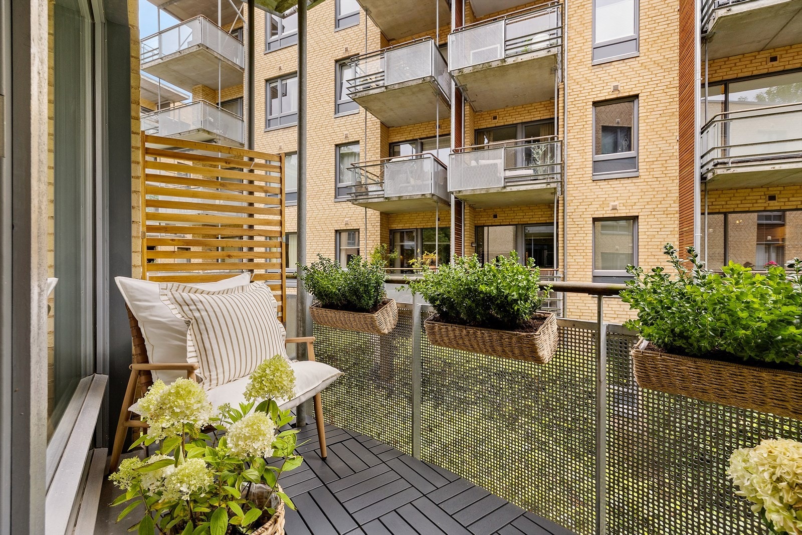 Balkongen vender ut mot grønne og tilbaketrukne omgivelser. Nytt terrassebelegg fra 2025 gir uteplassen et pent uttrykk. Galleribilde