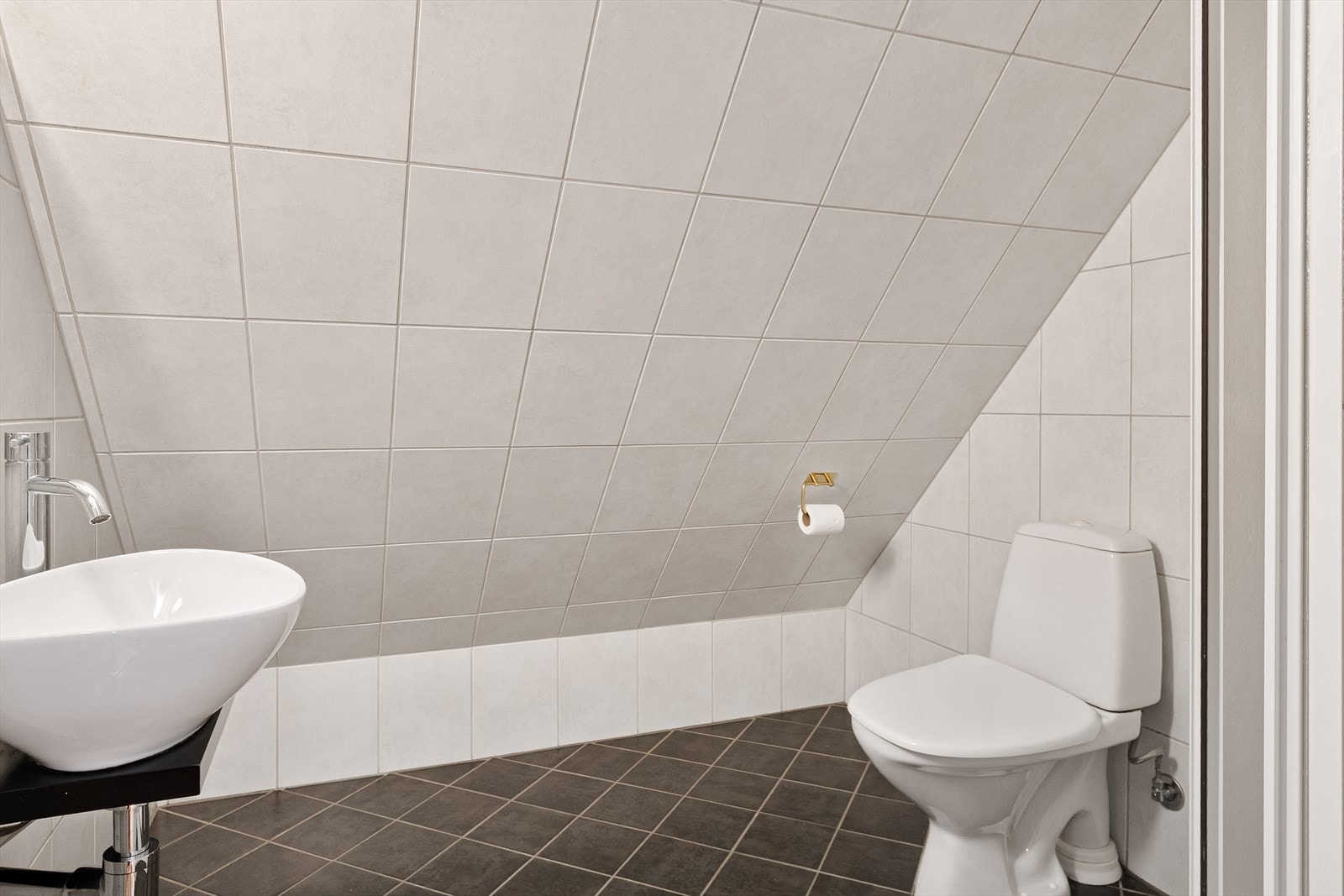 Badet i loftsetasjen har fliser på gulv, vegger og skråhimling, samt malte plater i himling. Galleribilde