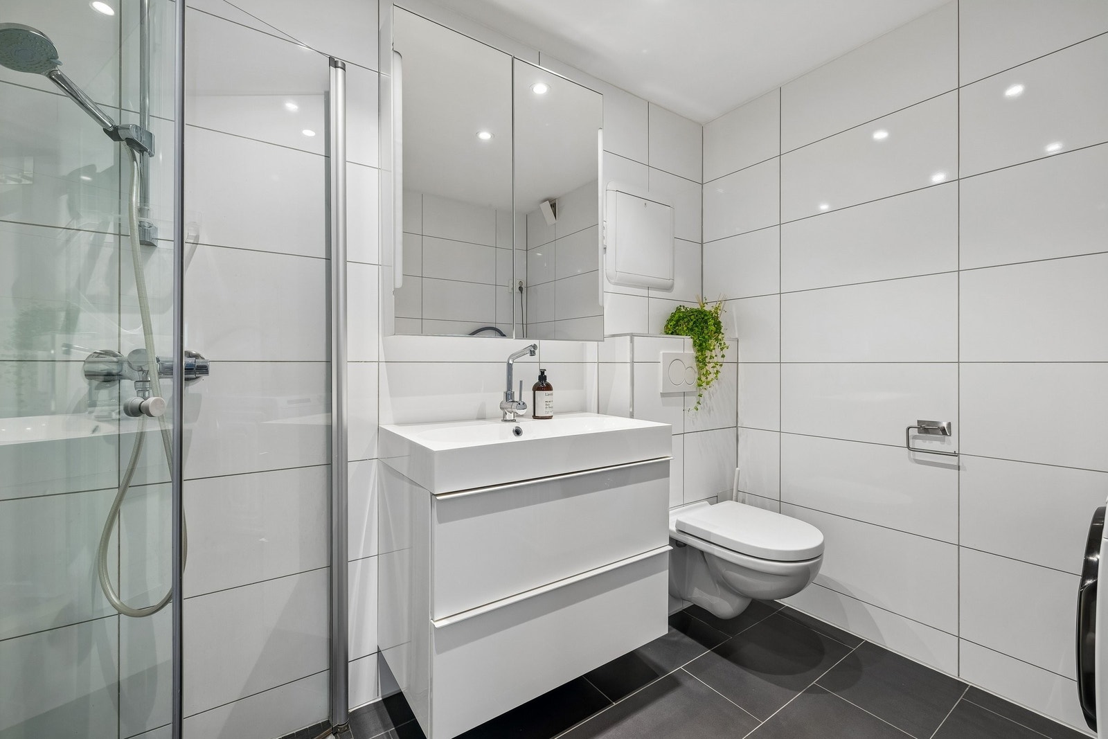 Badet gir et delikat inntrykk med downlights, sorte gulvfliser og hvite veggfliser. Galleribilde