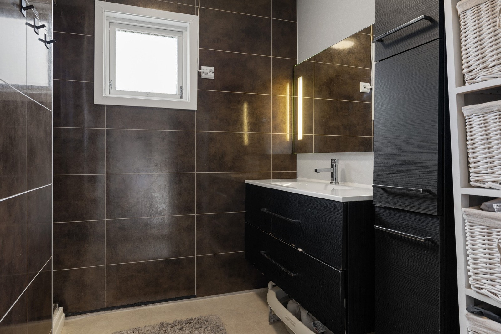 Badet i hovedetasjen har belegg på gulvet og på veggene er det våtromsplater. Innredning med mørke fronter, helstøpt servant og speil med belysning over. Galleribilde