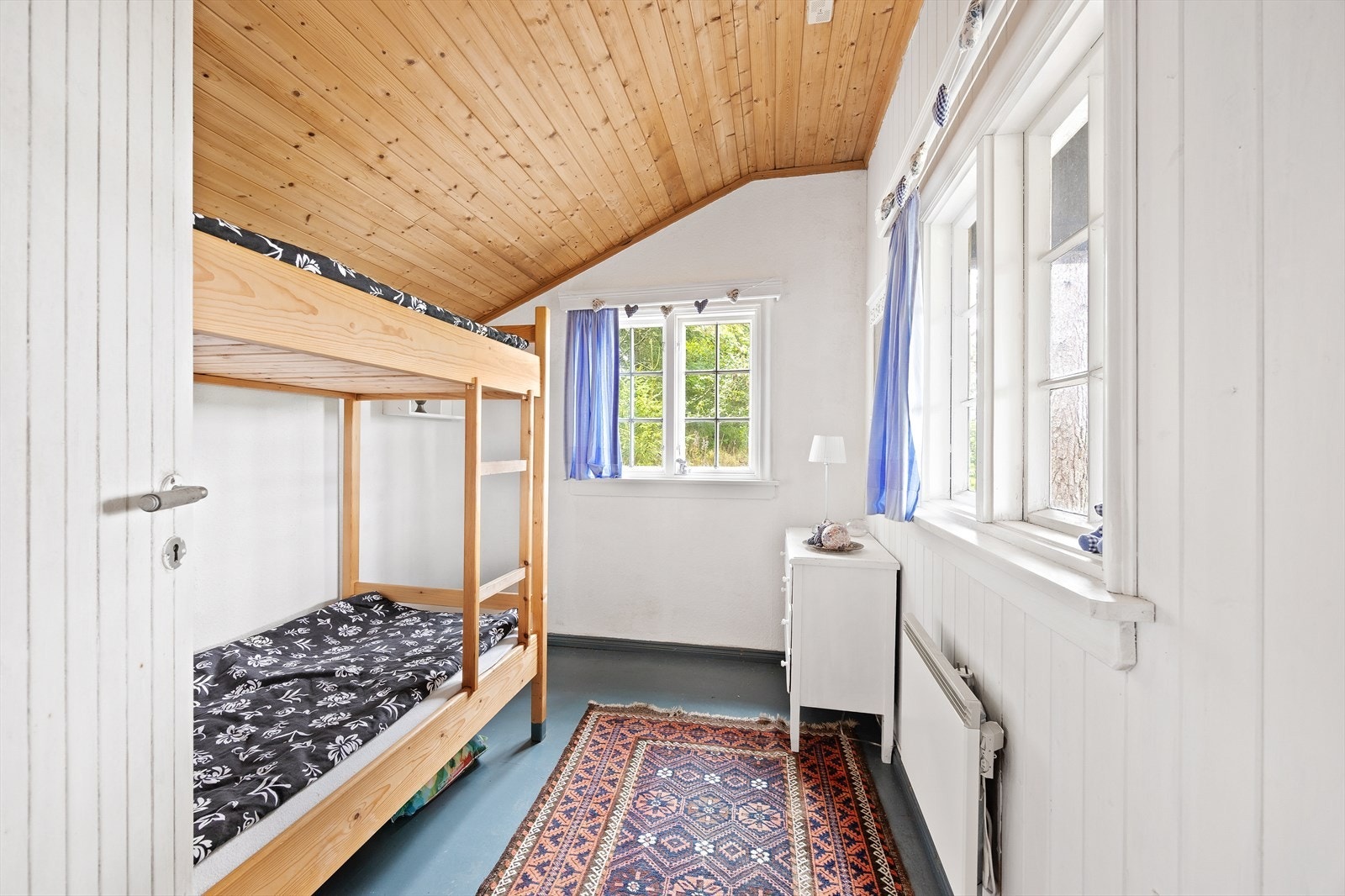 Annekset har hvitmalt panel på veggene, to doble sprossevinduer og blåmalt gulv. Galleribilde