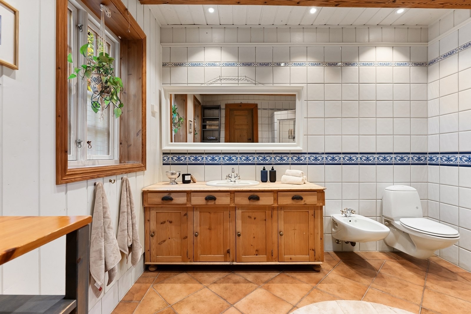 Romslig baderom med et gjennomført, tradisjonelt uttrykk og flere detaljer som gir rommet særpreg. Badet har flislagt gulv med varmekabler, mens veggene er utført med en kombinasjon av hvit panel og lyse fliser. Galleribilde