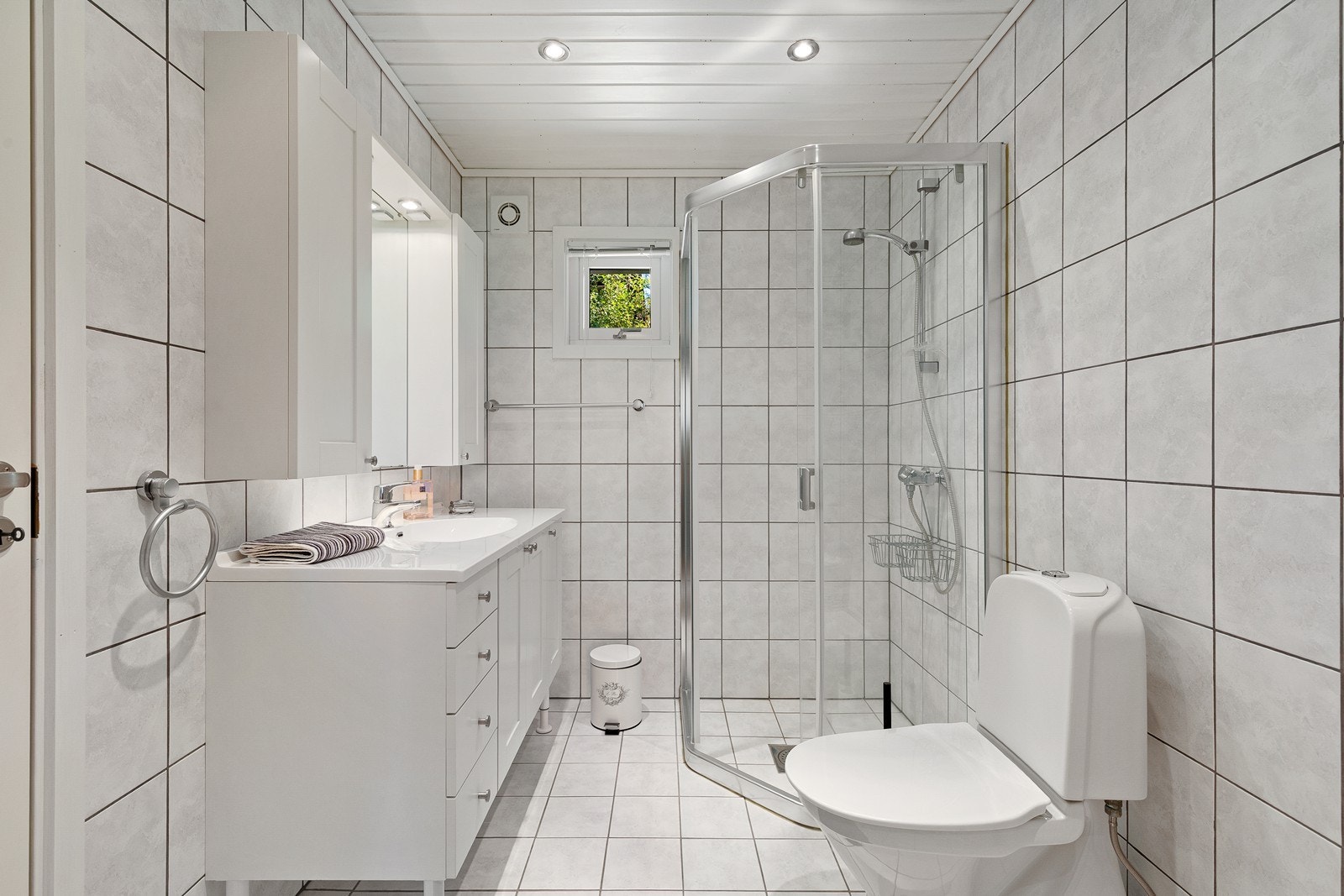 Badet har flislagd golv og veggar, samt varmekablar i golv. Her har du innreiing med servant, speil og overskap, dusjhjørne og toalett. Galleribilde