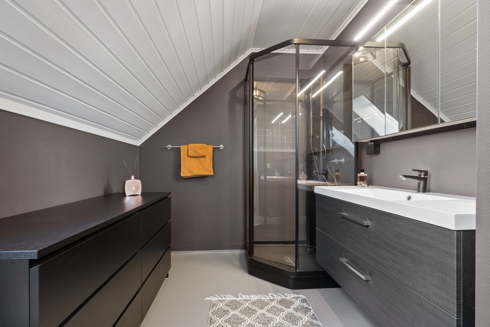 Badet er romslig, delikat og smakfullt innredet med en moderne innredning som gir rommet et tidløst uttrykk. Mørke fronter, lyse overflater og stilrene detaljer skaper en elegant kontrast, samtidig som rommet oppleves harmonisk og innbydende. Galleribilde