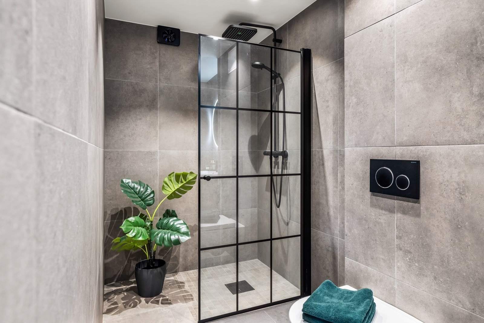 Badet er flislagt i en elegant gråtone og innredet med romslig servantinnredning med skuffer, stort rundt speil med integrert belysning og vegghengt toalett. Galleribilde