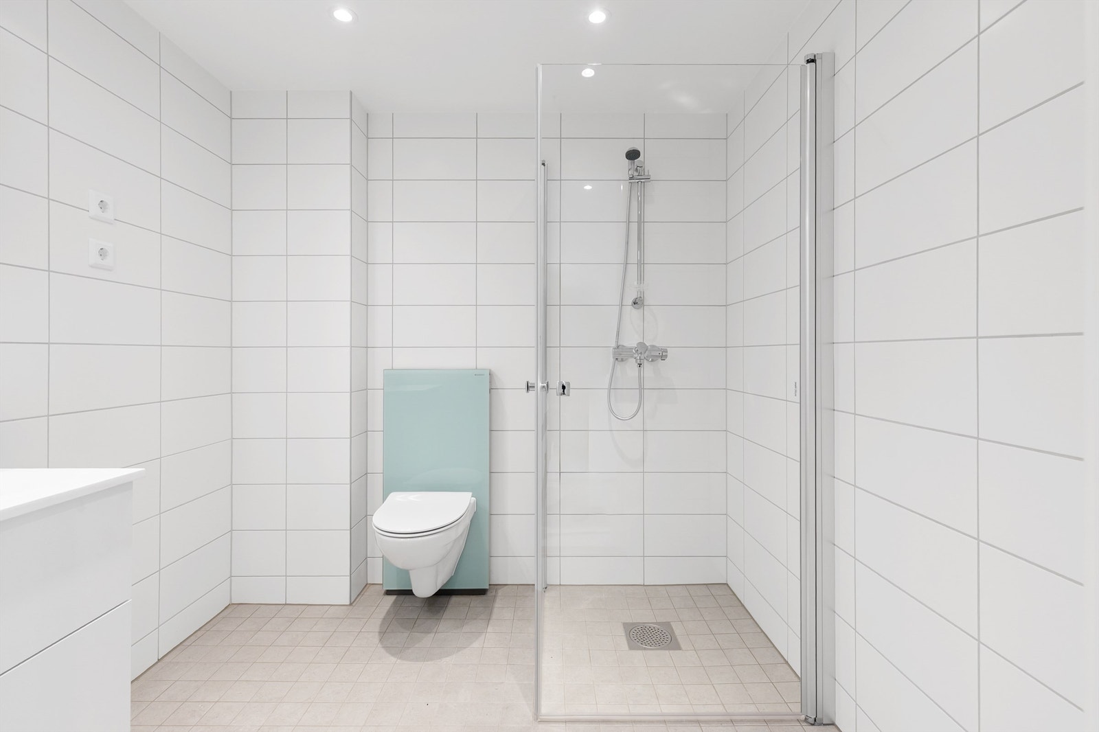 Det er pent flislagt bad på gulv og vegger med elektrisk gulvvarme. Badet er innredet med vegghengt klosett, dusjhjørne med glassdører, servantskap med servant og speilskap med overbelysning. Galleribilde