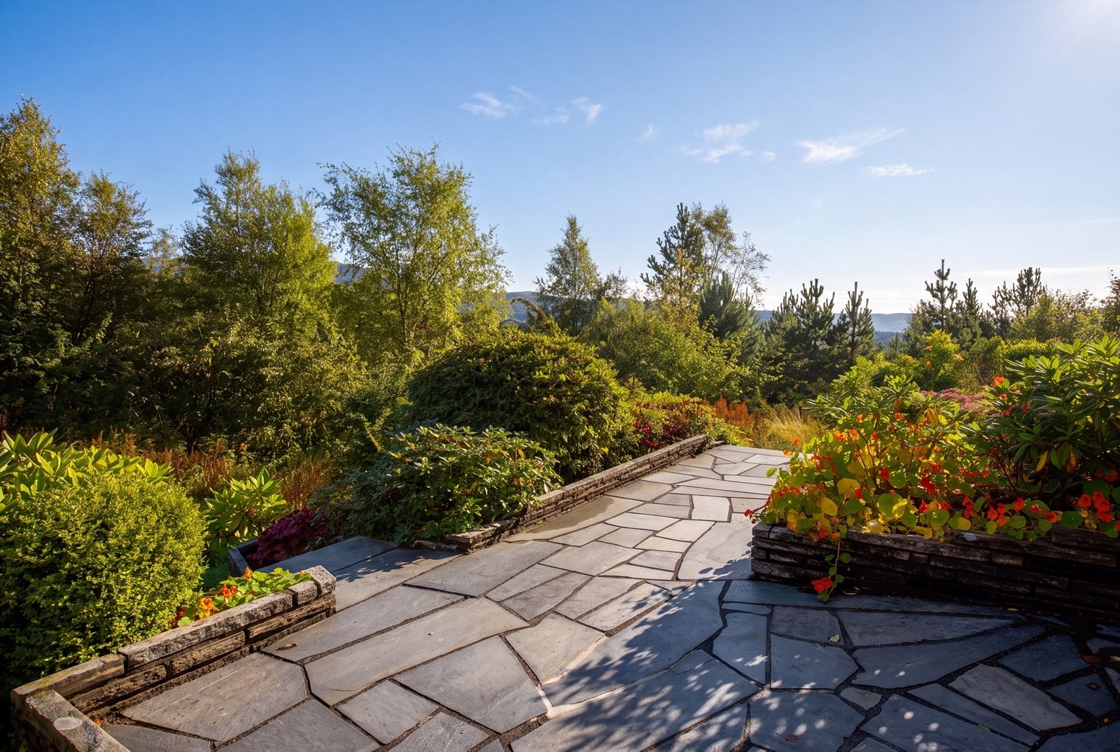 Skiferbelagt uteplass med blomsterkasser i naturstein og utsikt mot omkringliggende natur. Galleribilde