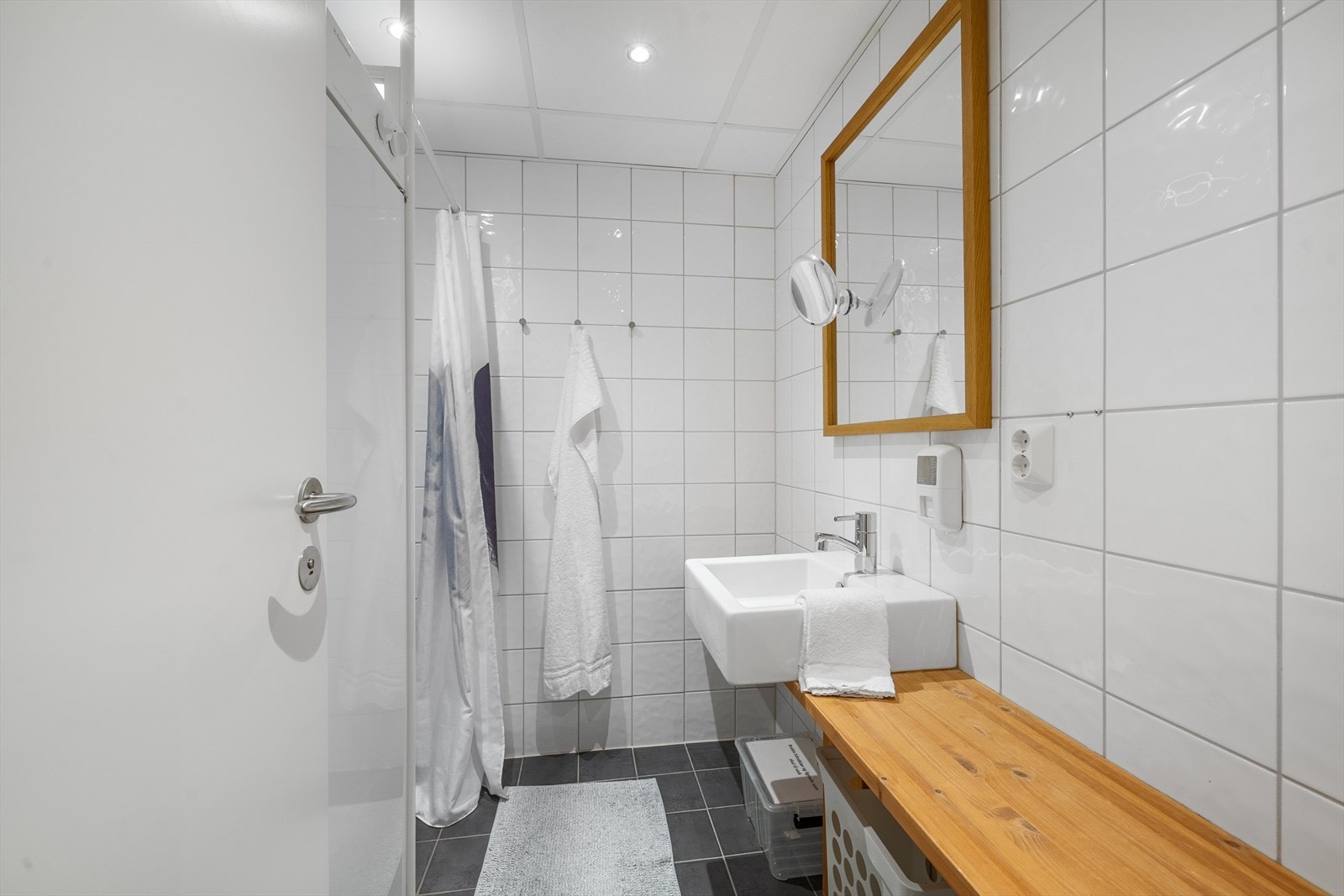 Badet har hvite keramiske veggfliser, mørkt flisgulv og innfelte downlights. Galleribilde