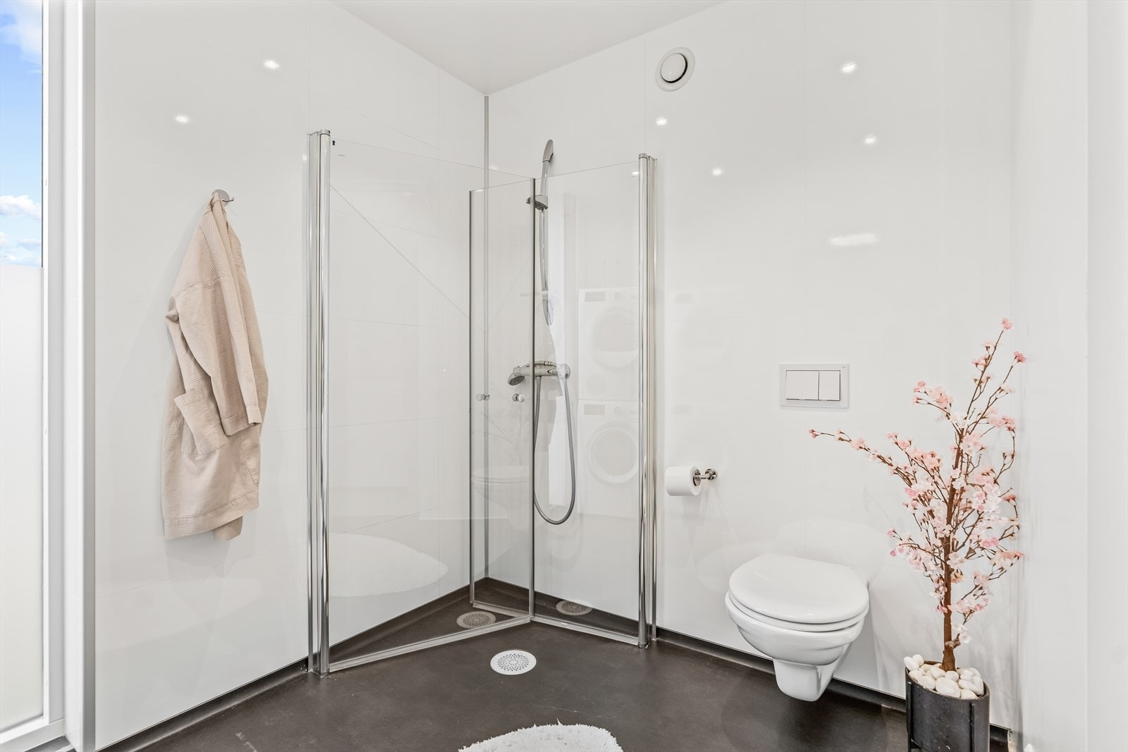 Videre har badet innredning med nedfelt servant, veggmontert toalett, dusjvegger/hjørne og opplegg for vaskemaskin. Galleribilde