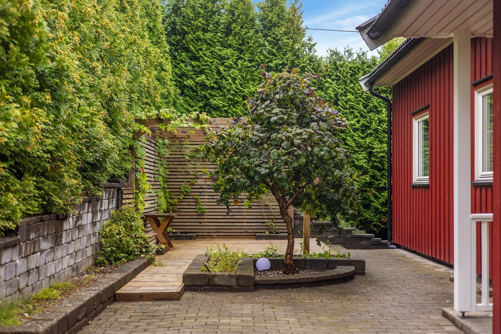Gårdsplassen er opparbeidet med belegningsstein og omkranset av tett hekk. Galleribilde