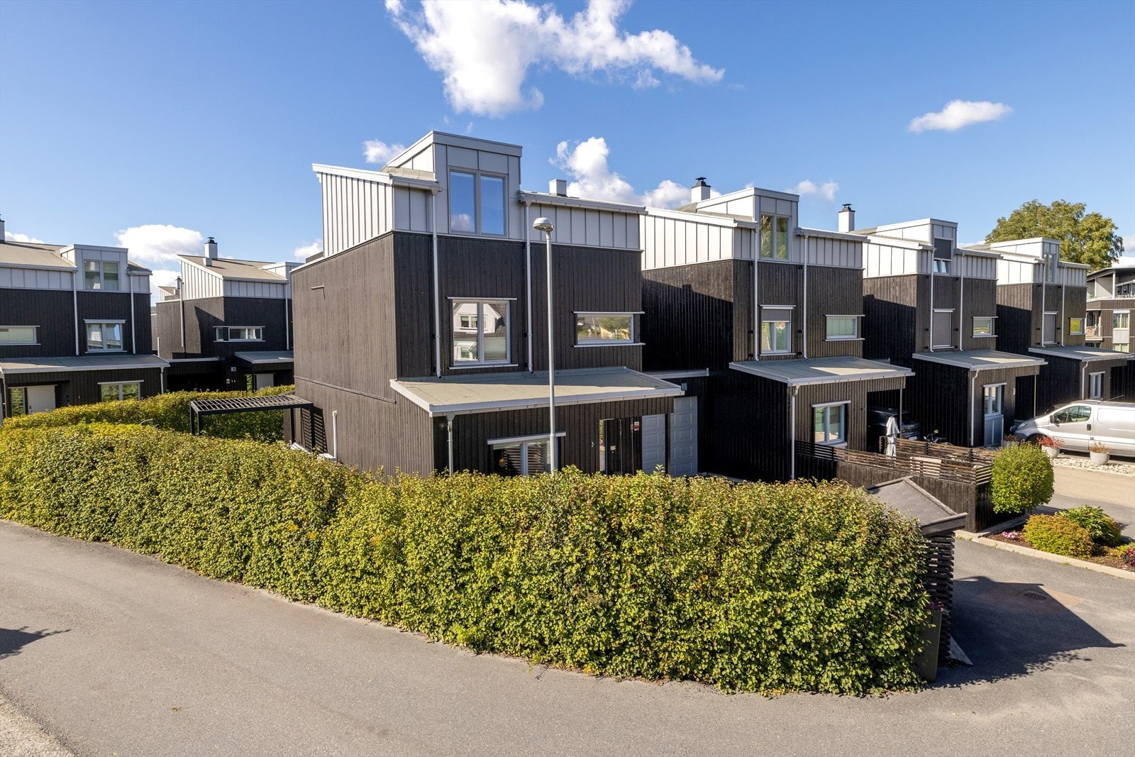Boligrekken sett fra adkomstsiden med asfaltert gårdsplass og hekk. Galleribilde