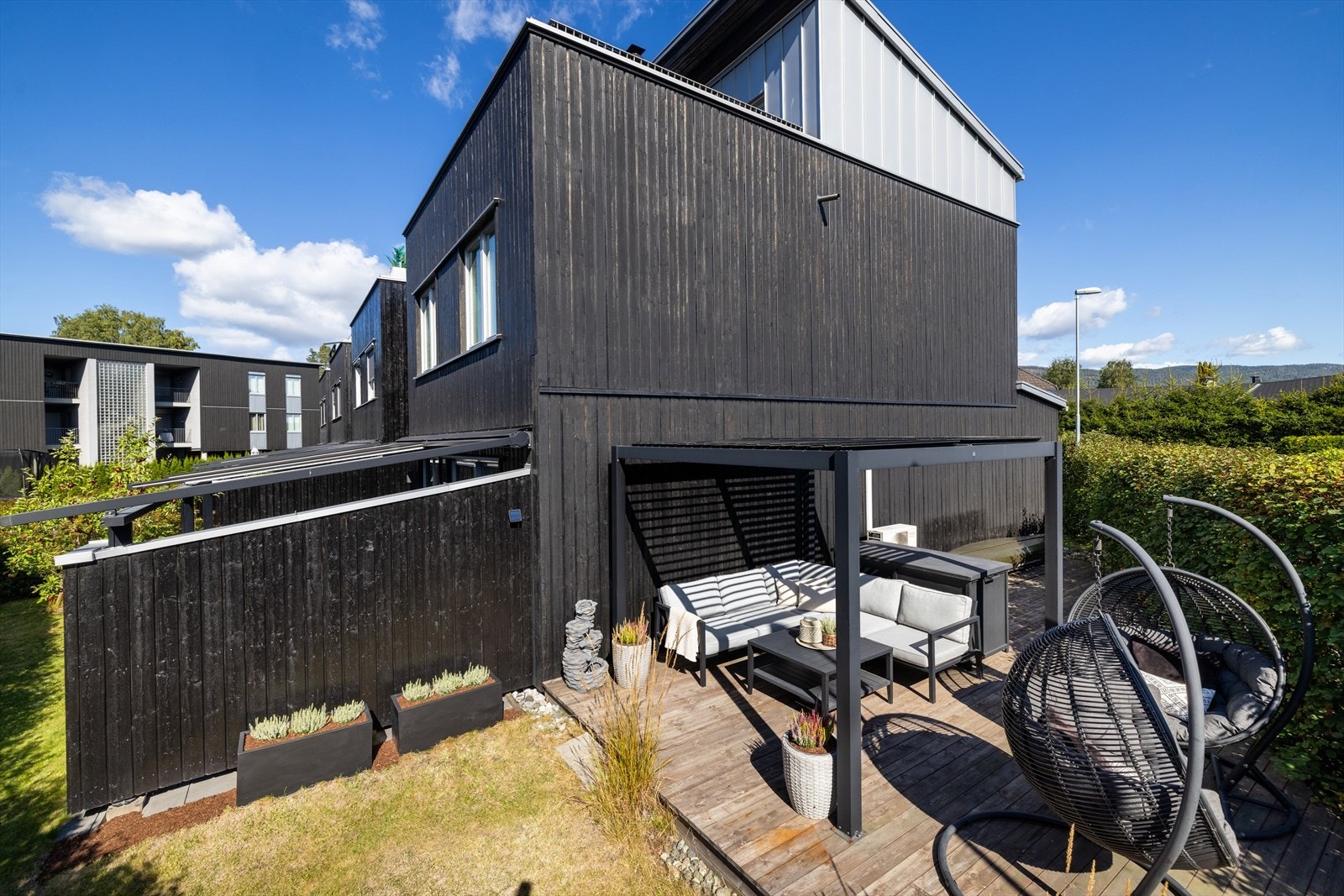 Boligens moderne fasade i mørk stående trekledning og helhetlige uteområder. Galleribilde