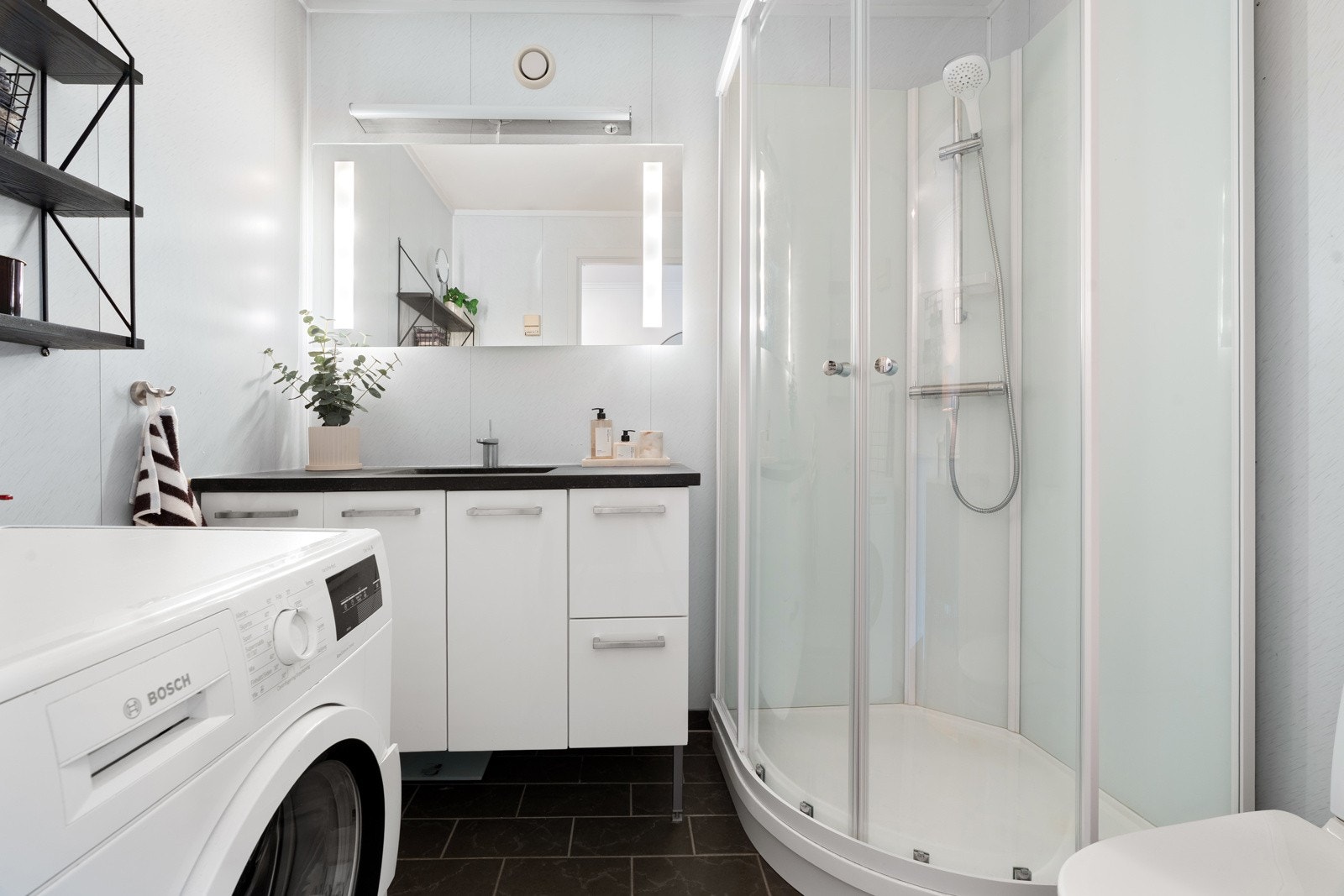Badet har flislagt gulv, nedfelt servant med innredning, toalett, opplegg til vaskemaskin og dusjkabinett. Dusjkabinettet og dusjbatteri ble skiftet profesjonelt i 2026 av Comfort.