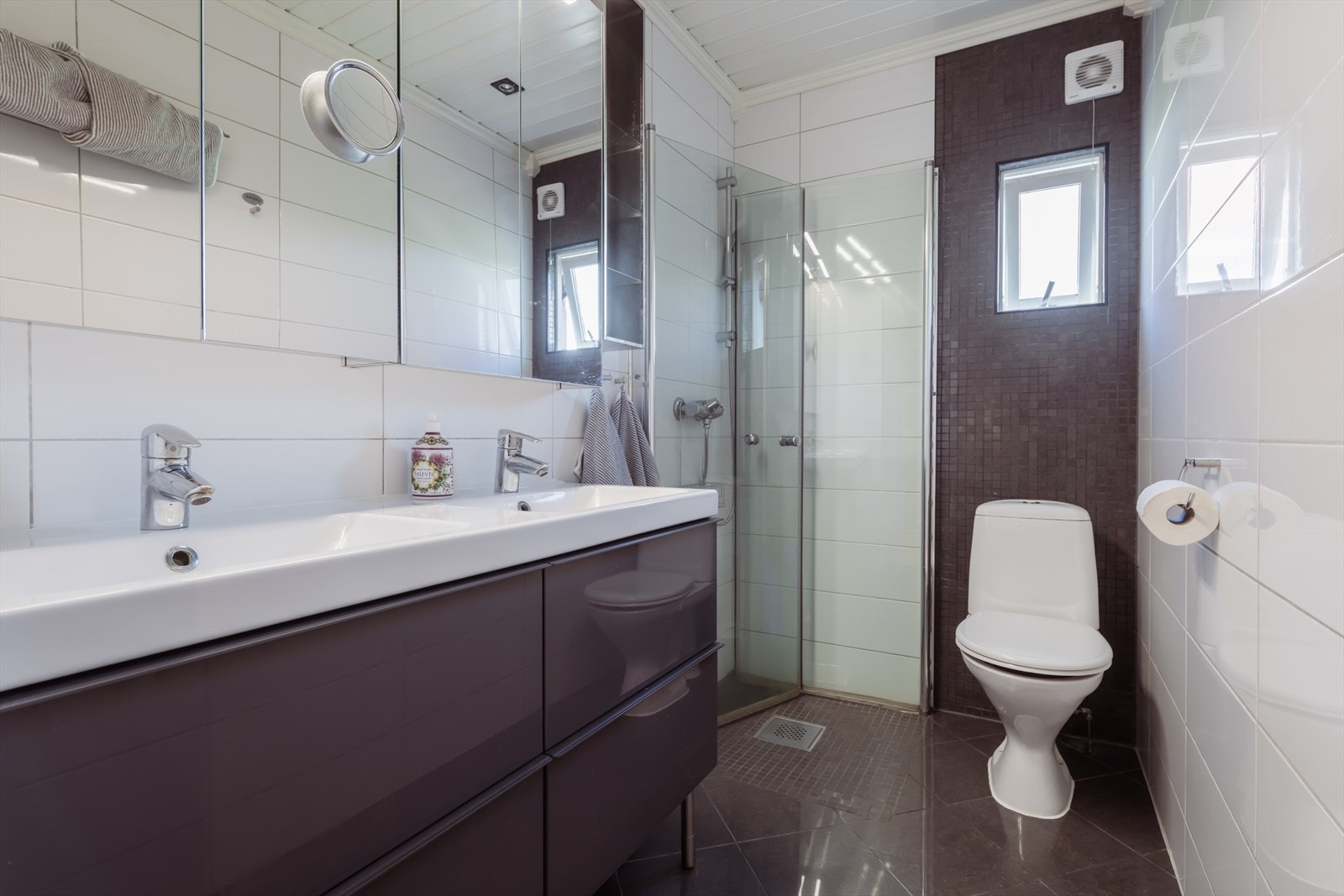 Badet i 1 etasje har vegger av keramiske fliser og mosaikkfliser, lagt over opprinnelige fliser i ca. 2012 og gulv av keramiske fliser lagt over opprinnelige fliser i ca. 2012. Rommet har dusjhjørne med glassvegger og dører, servant med skap og toalett. Galleribilde