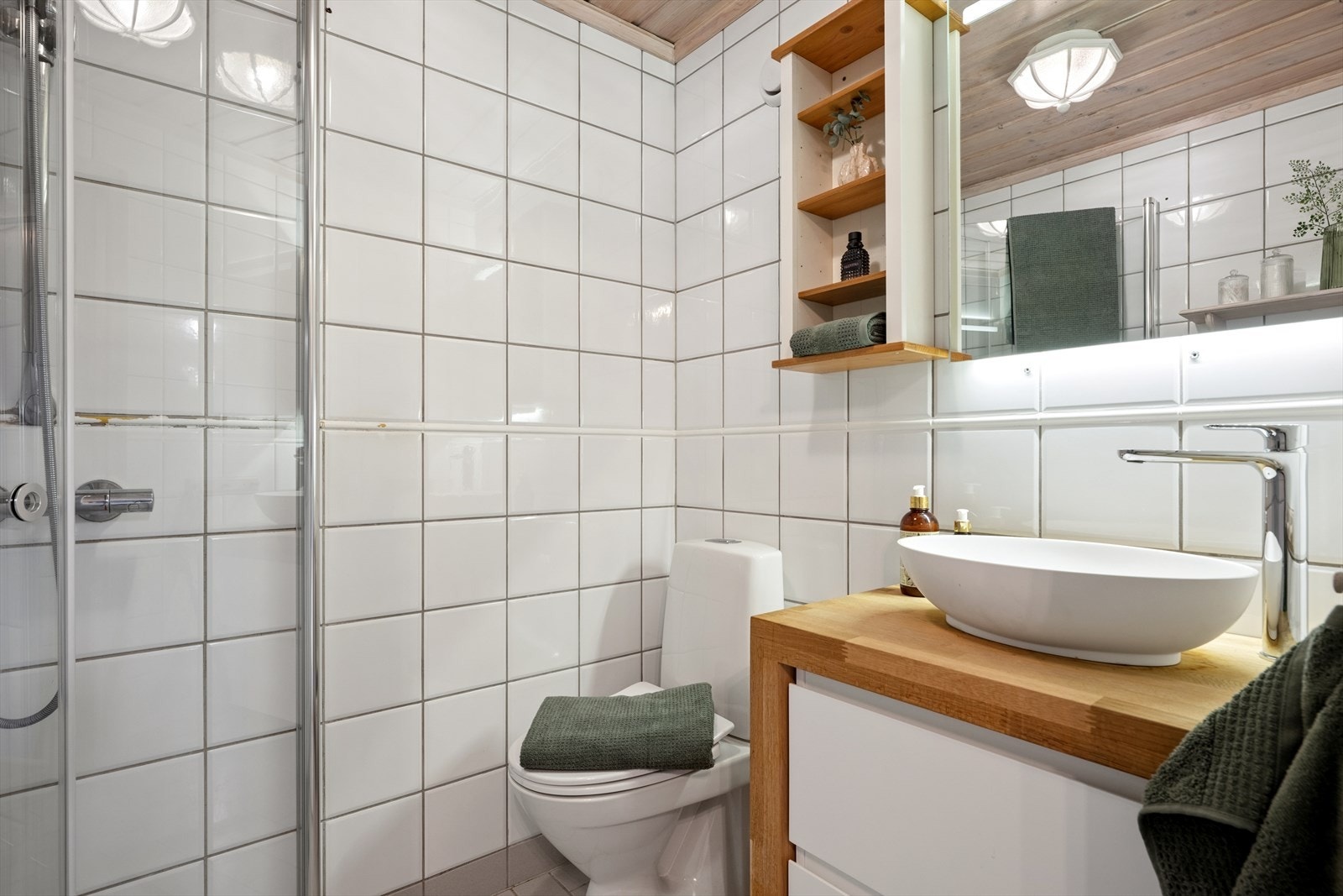 Badet i underetasjen er et lyst og funksjonelt bad med flislagte overflater, dusjkabinett og servantinnredning med god oppbevaringsplass. Galleribilde