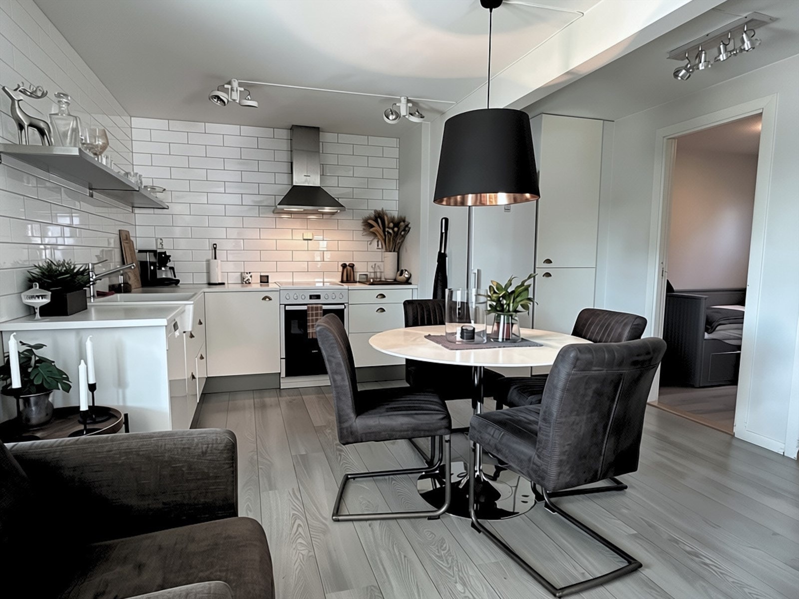 En lang, åpen stålhylle over benkeplaten gir praktisk oppbevaringsplass og tilfører en elegant kontrast til de hvite flisene. Kjøkkenet har spotbelysning i taket, vaskekum og oppvaskmaskin. Galleribilde