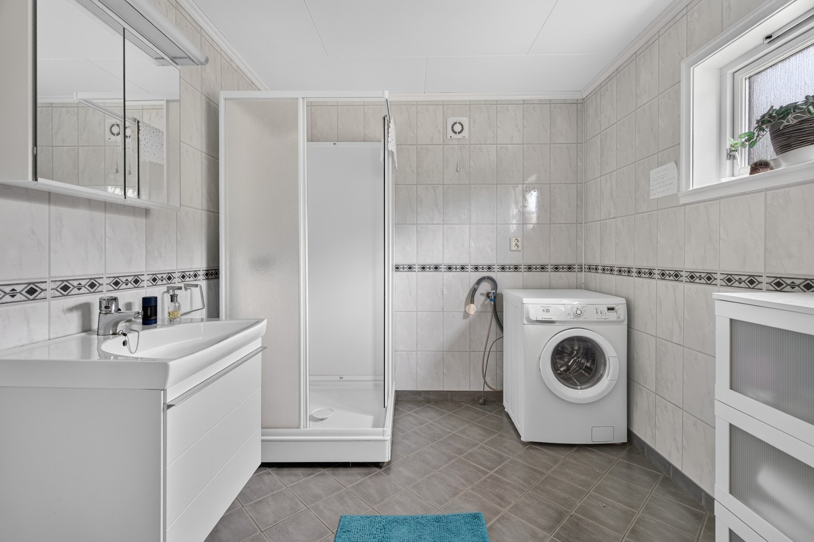 Badet er av god størrelse. Badet er utstyrt med dusjkabinett, seksjon med vask, toalett og opplegg for vaskemaskin. Galleribilde