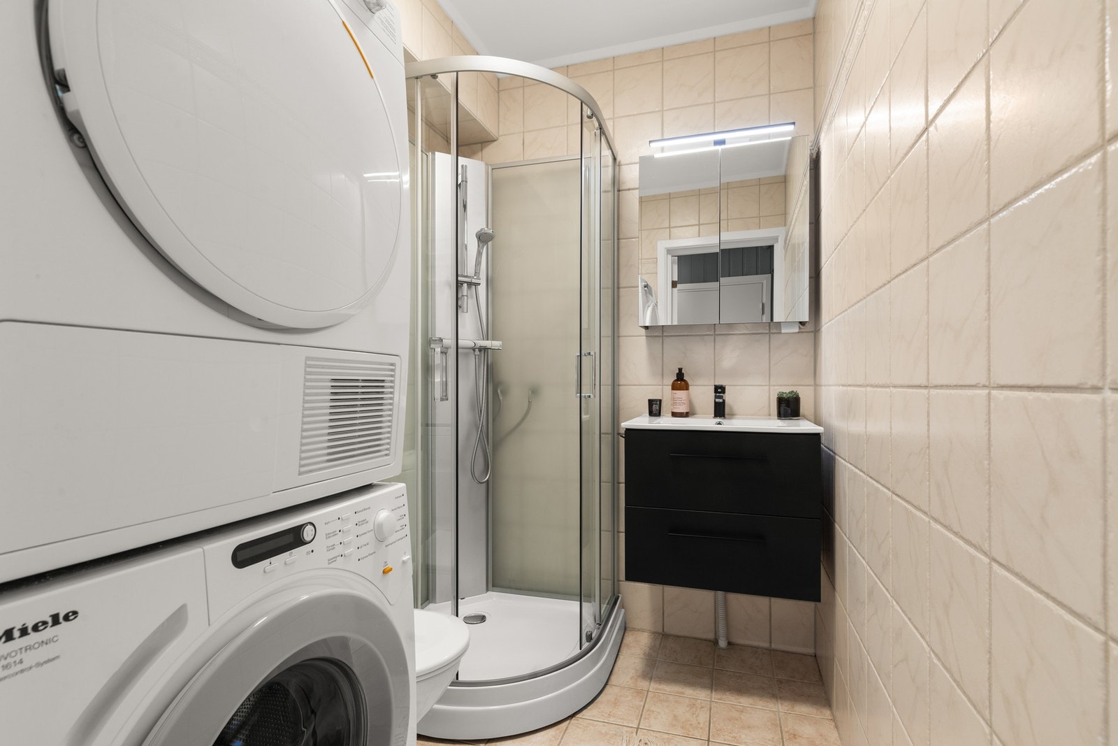 Videre er det opplegg for vaskemaskin og tørketrommel. Det er opplyst at dusjkabinett, servantseksjon og speilskap ble skiftet ut i 2023. Badet har naturlig ventilasjon. Galleribilde